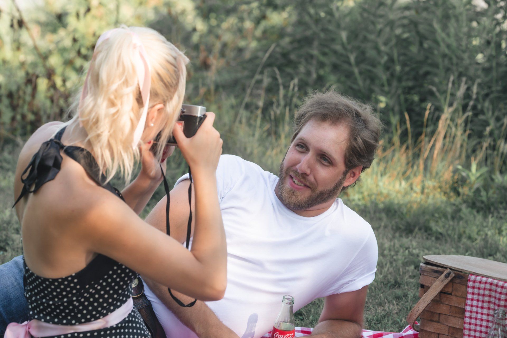A woman is taking a picture of a man on a picnic blanket.