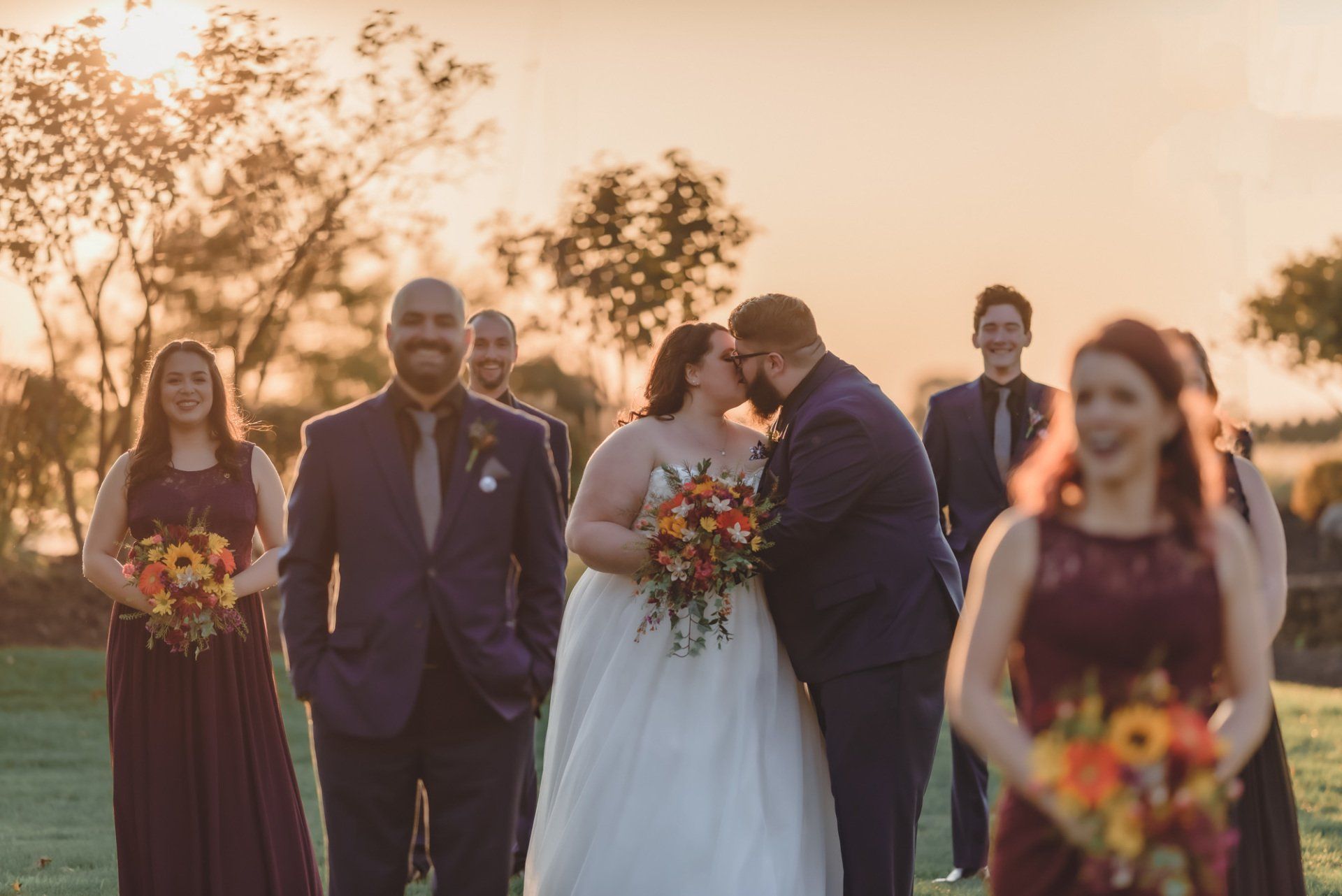 A bride and groom are kissing in front of their wedding party.