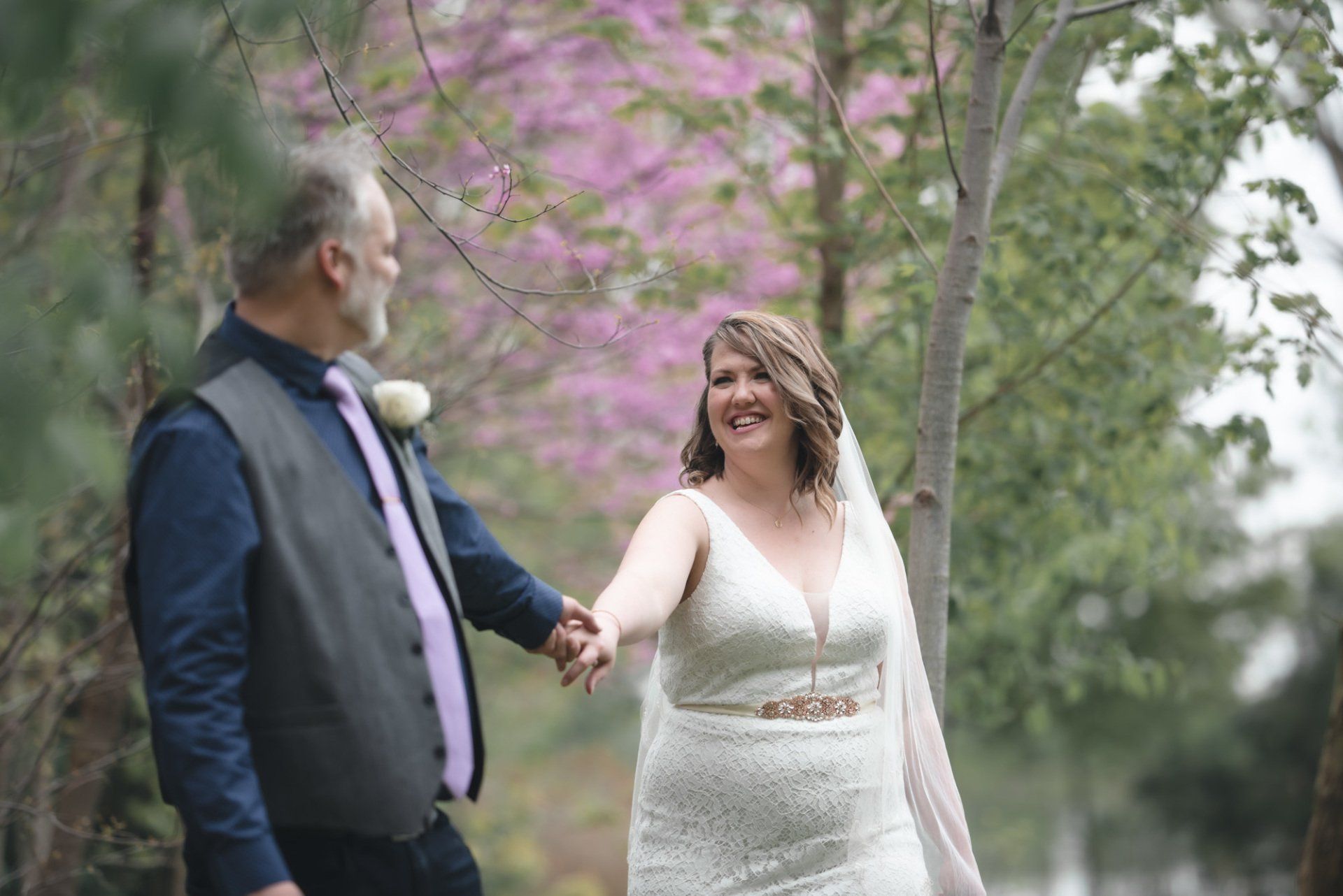 A bride and groom are holding hands while walking in a park.