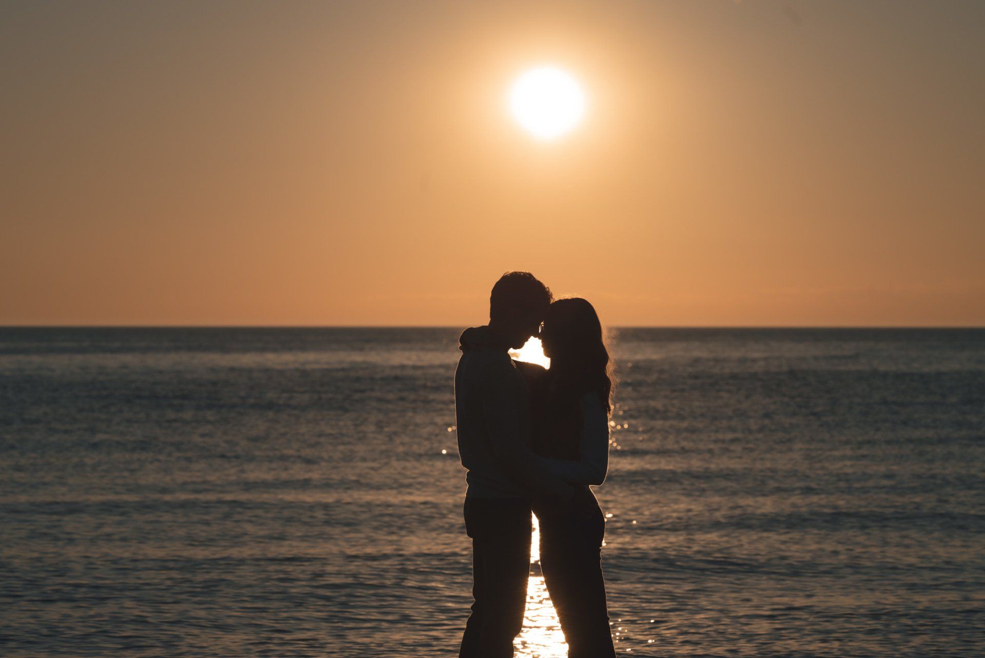 A man and a woman are kissing on the beach at sunset.