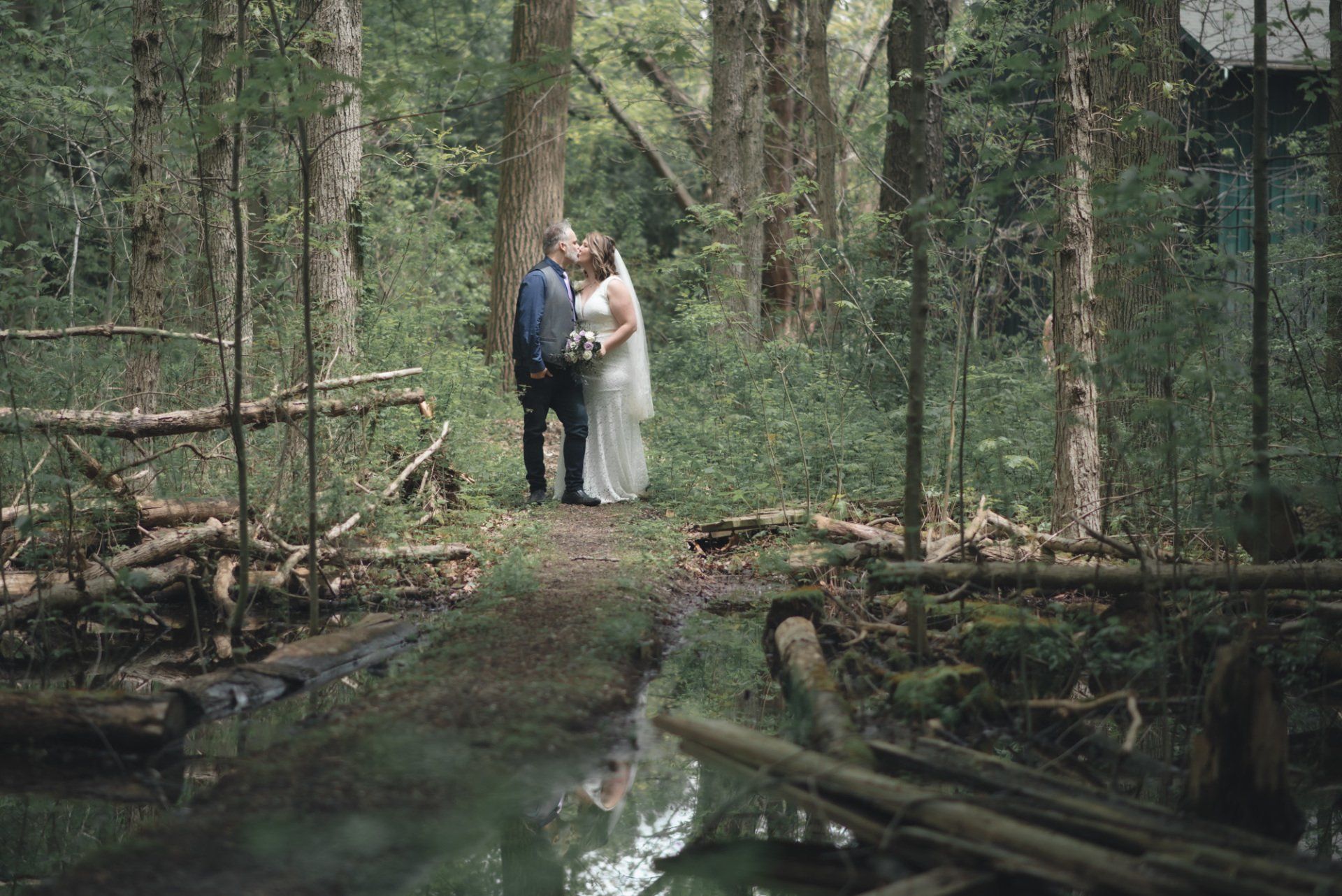 A bride and groom are kissing in the woods near a river.