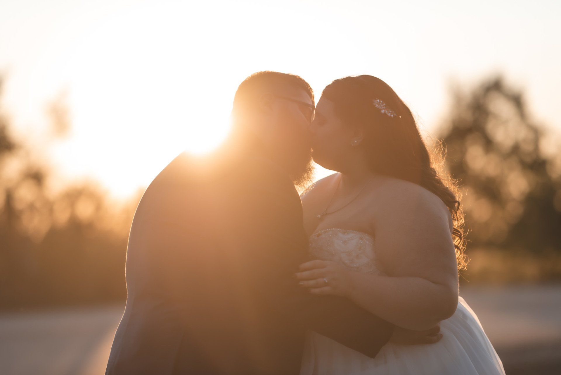 A bride and groom are kissing in front of the sun.