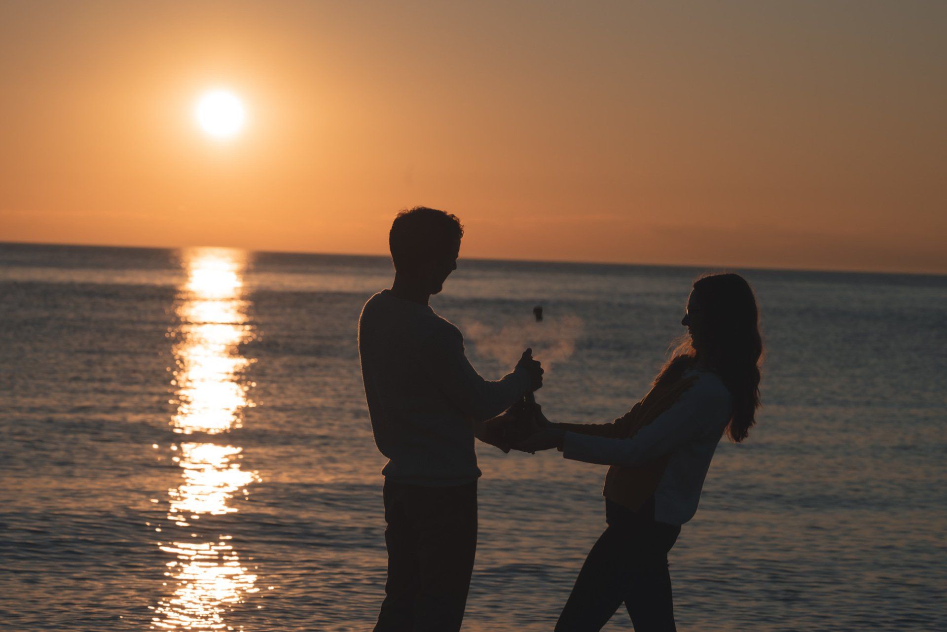 A man and a woman are dancing on the beach at sunset.