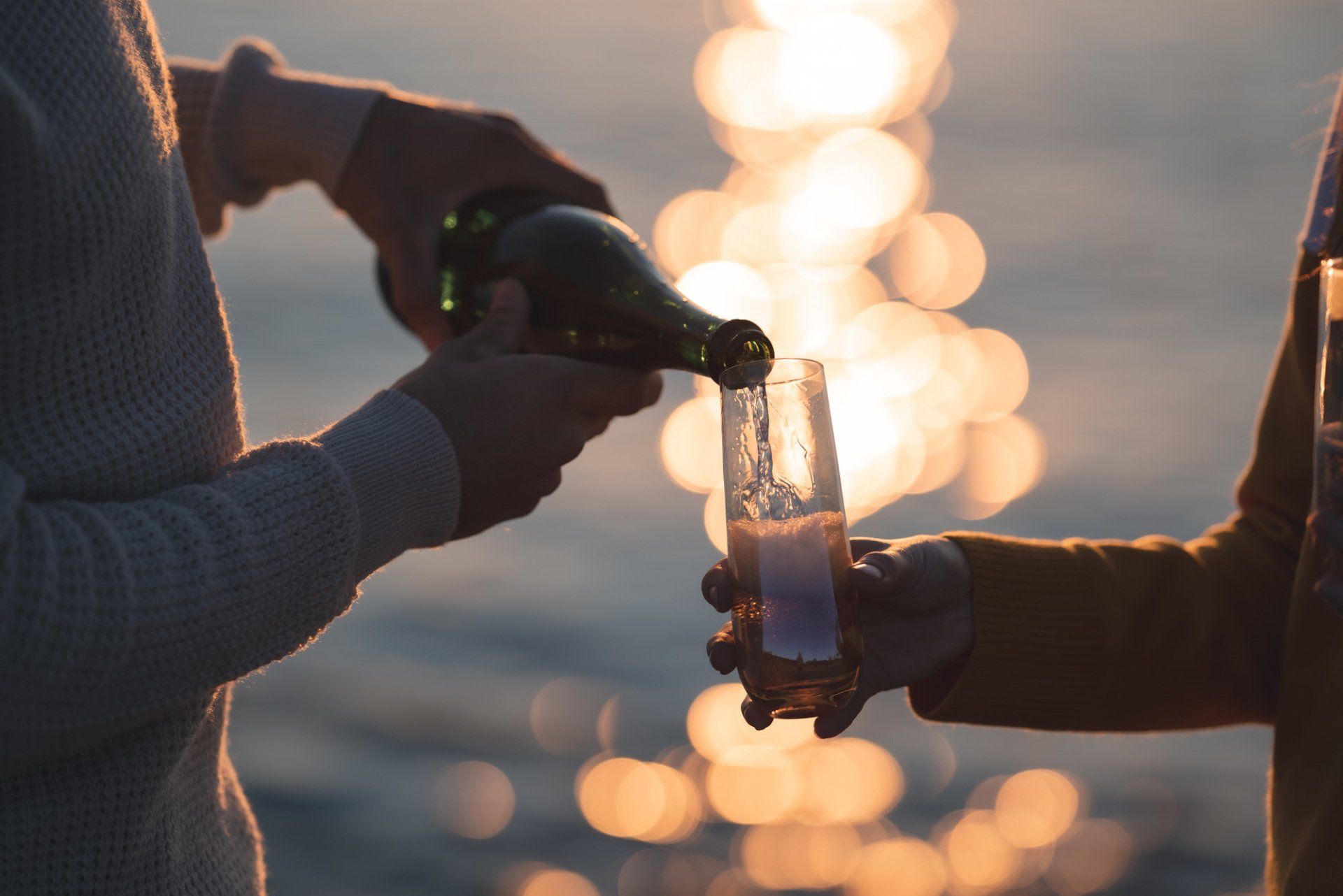 A man is pouring champagne into a glass on the beach.