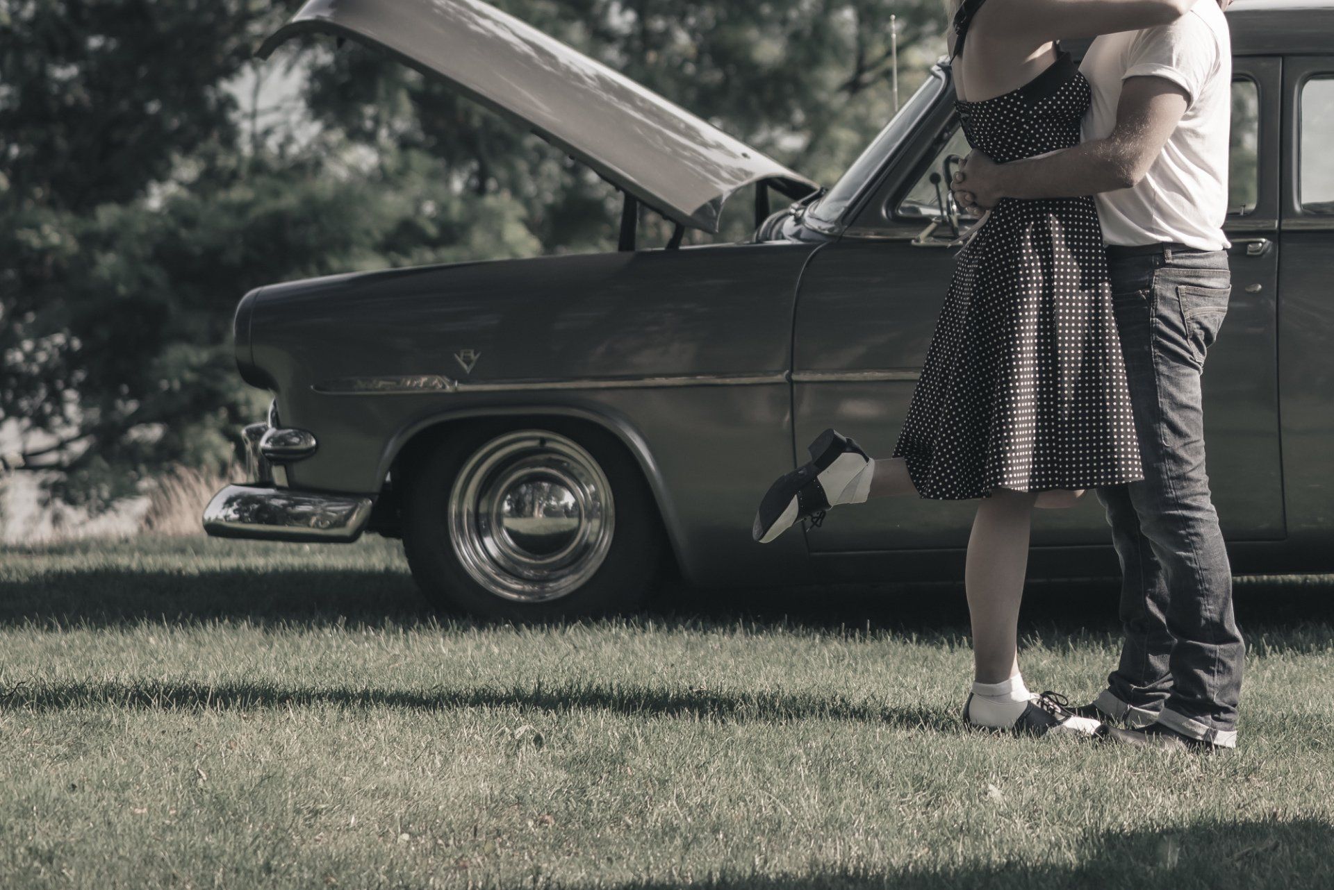 A man and a woman are hugging in front of a car with the hood up.