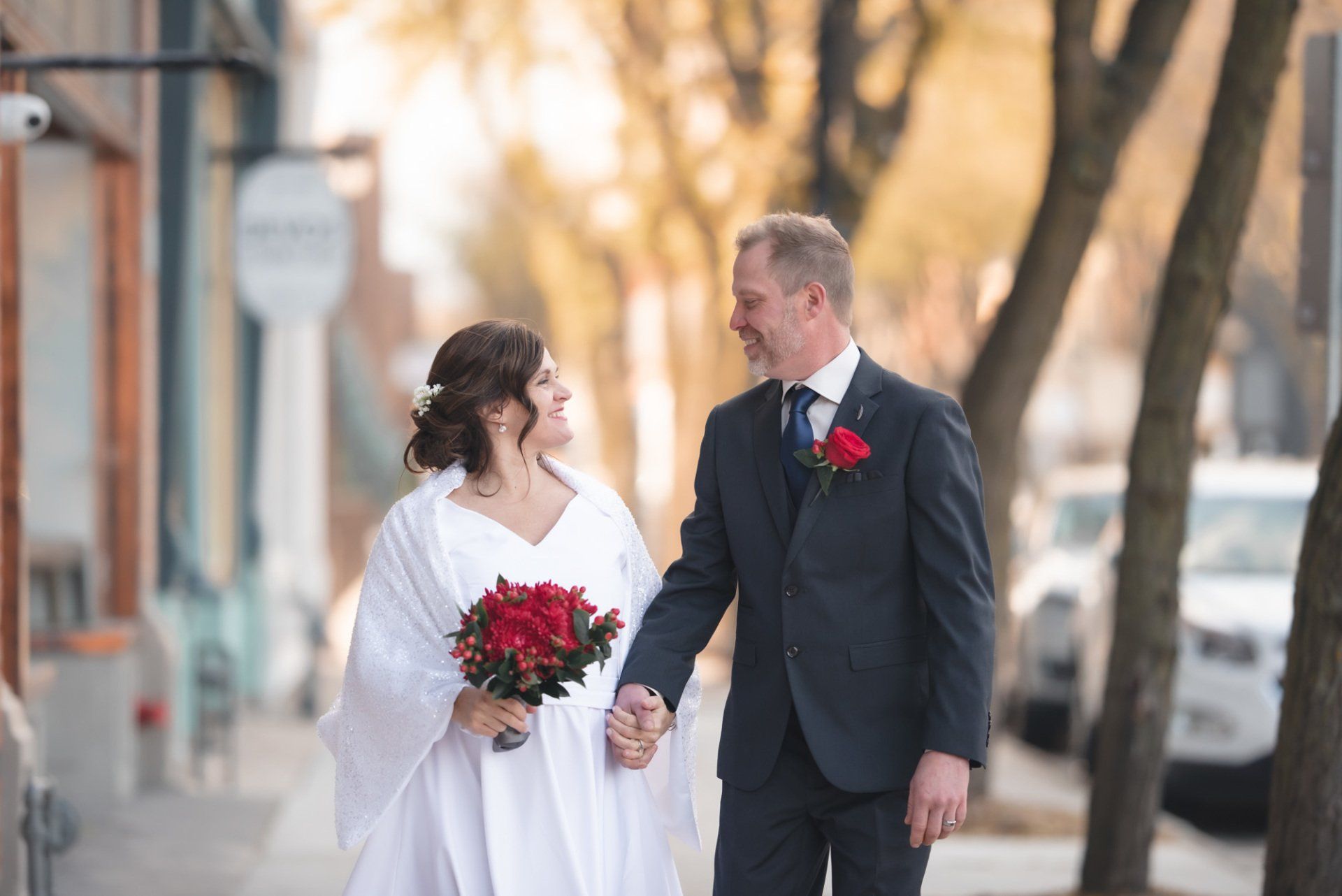A bride and groom are walking down the street holding hands.