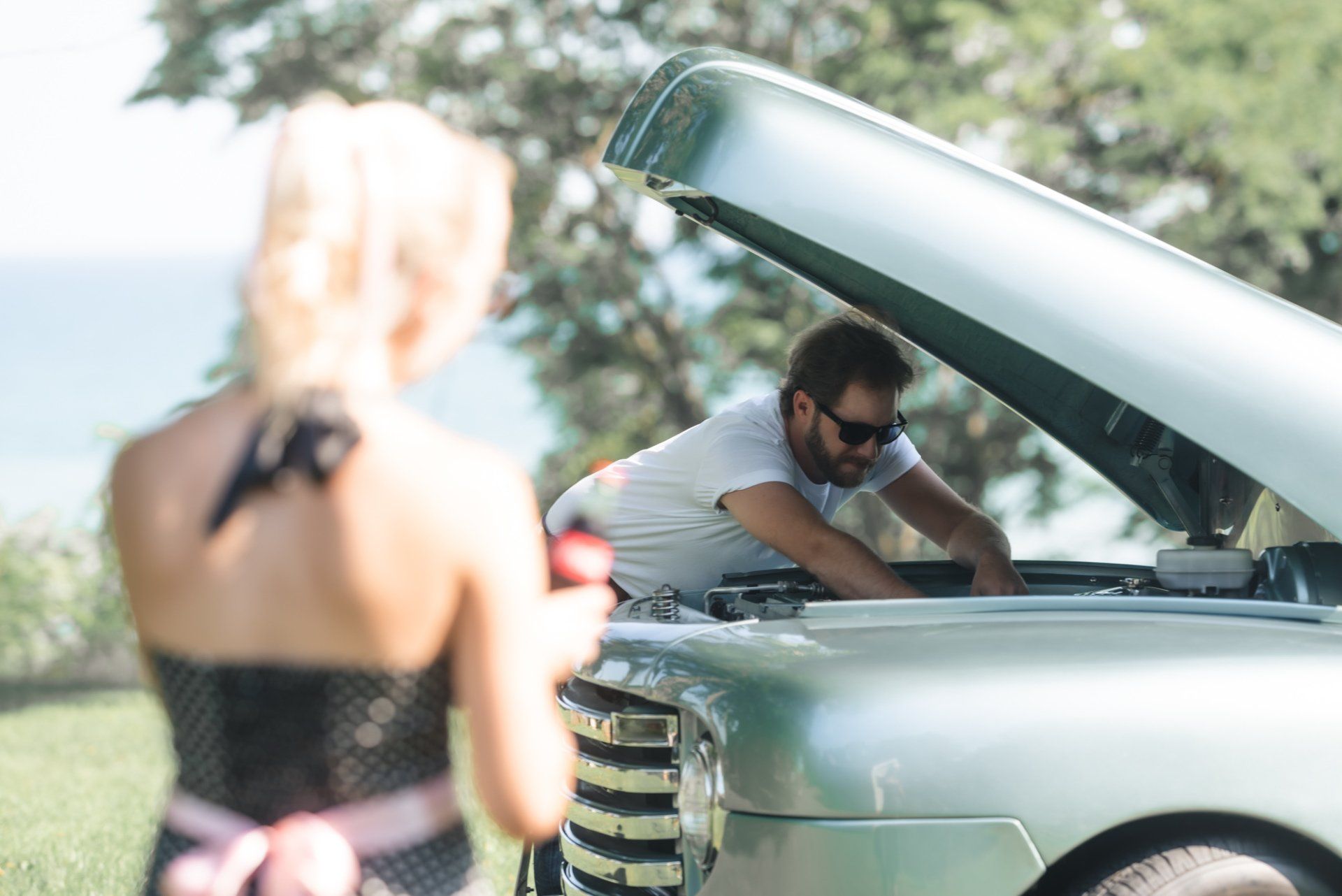 A woman is taking a picture of a man working on his car.
