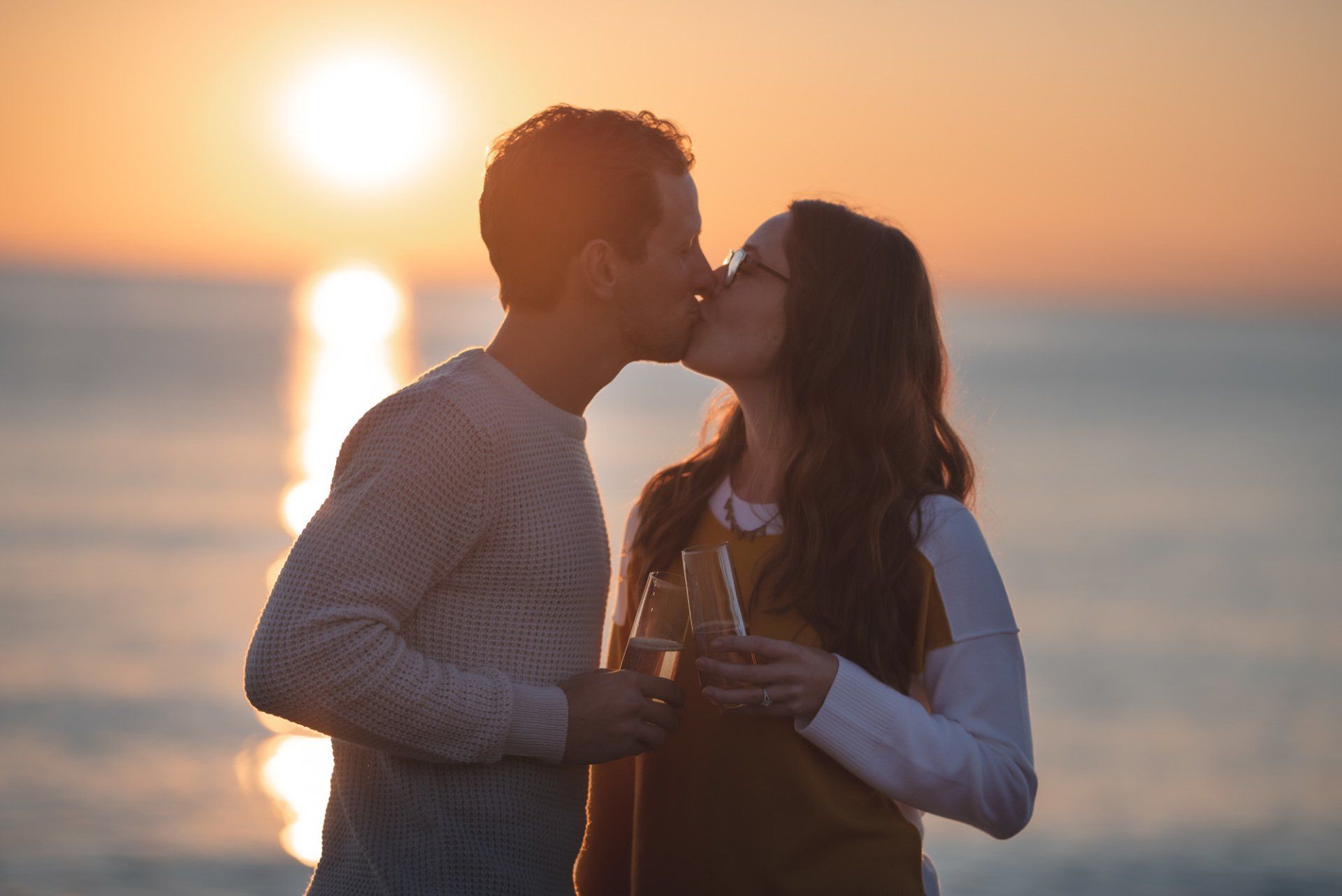 A man and a woman are kissing on the beach at sunset.