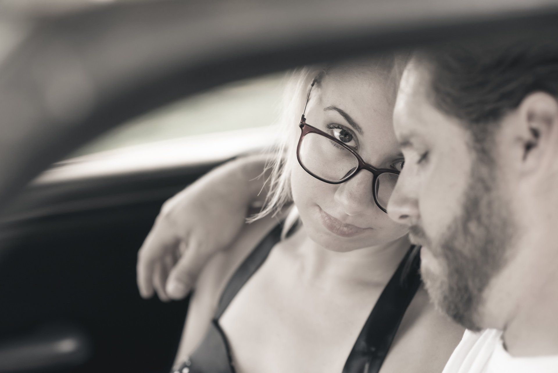 A man and a woman are sitting in a car and the woman is wearing glasses.