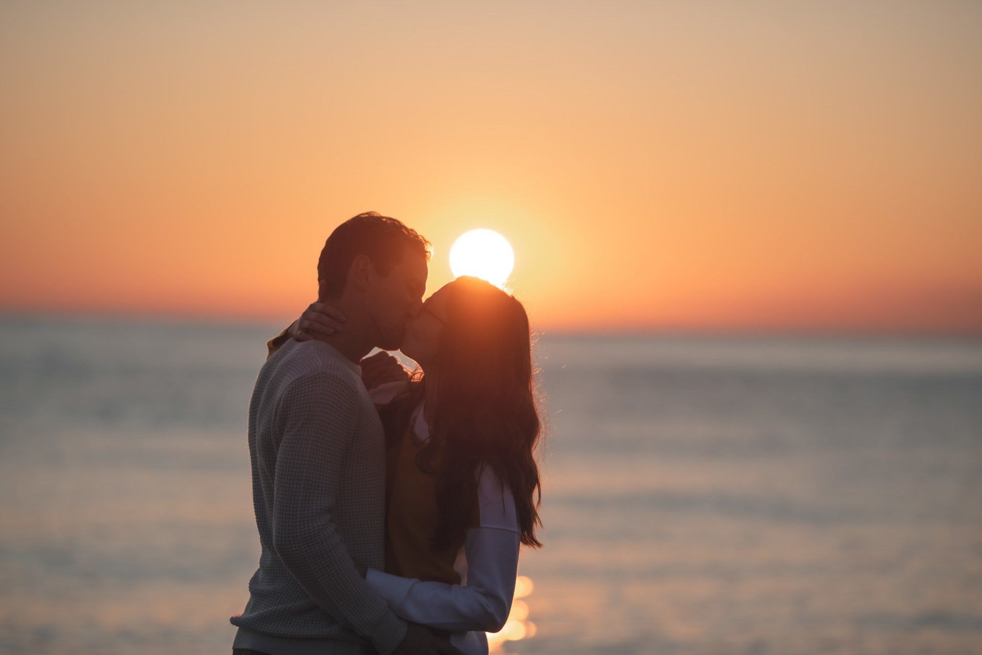 A man and a woman are kissing on the beach at sunset.