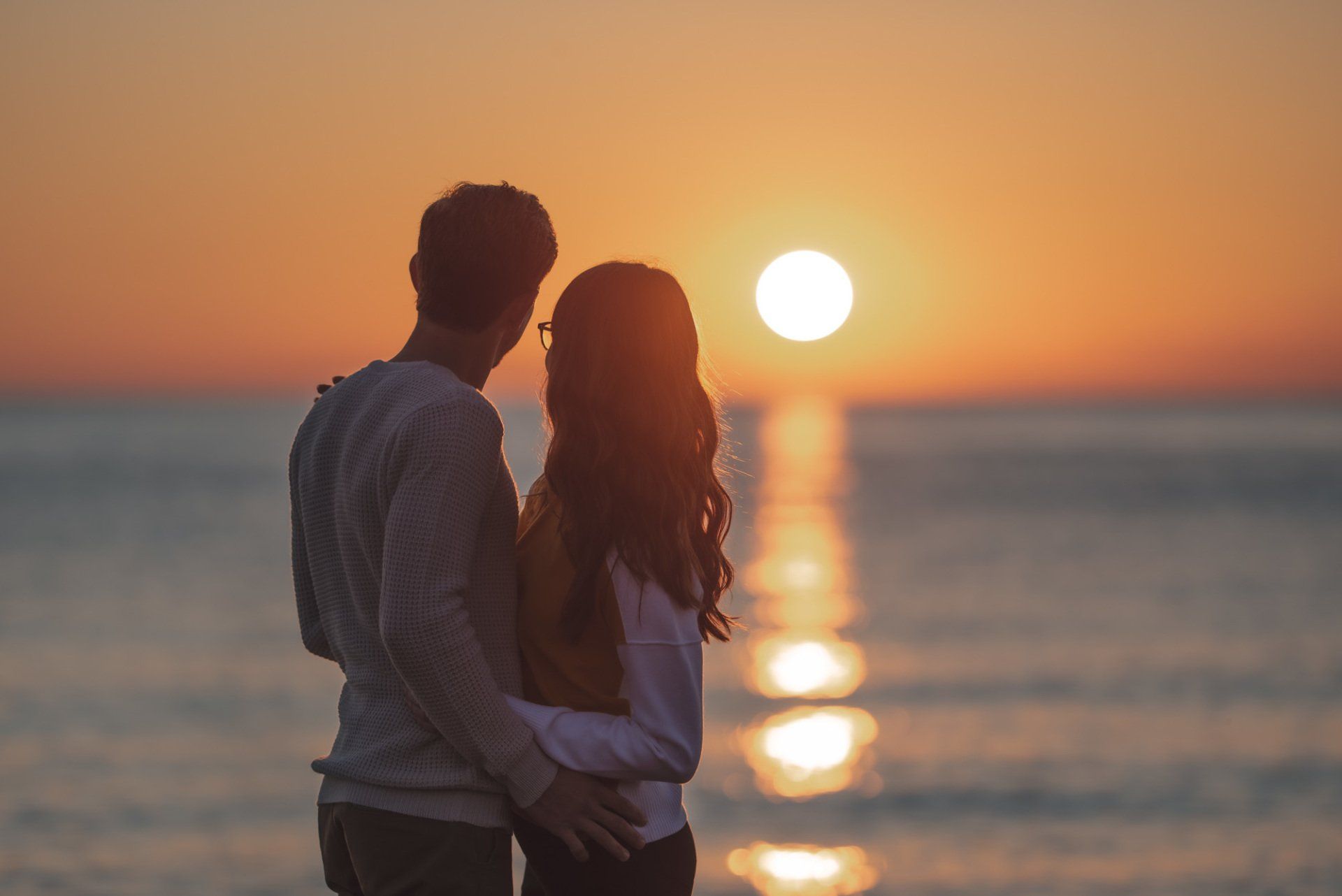 A man and a woman are standing on the beach looking at the sunset.