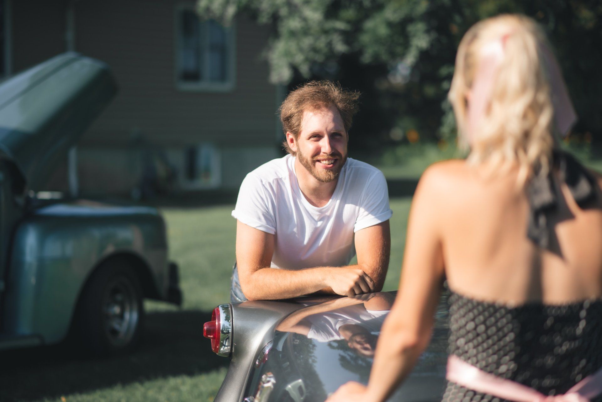 A man is sitting on the hood of a car next to a woman.