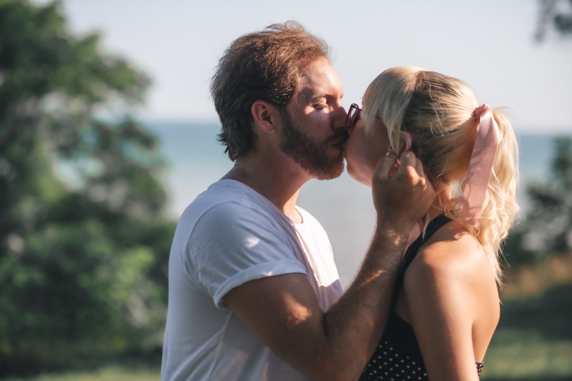 A man and a woman are kissing in front of the ocean.