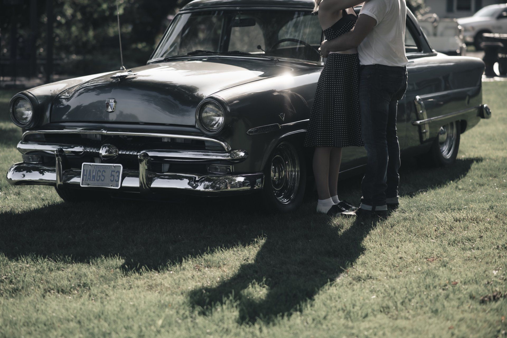 A man and woman standing in front of a car with a license plate that says a555