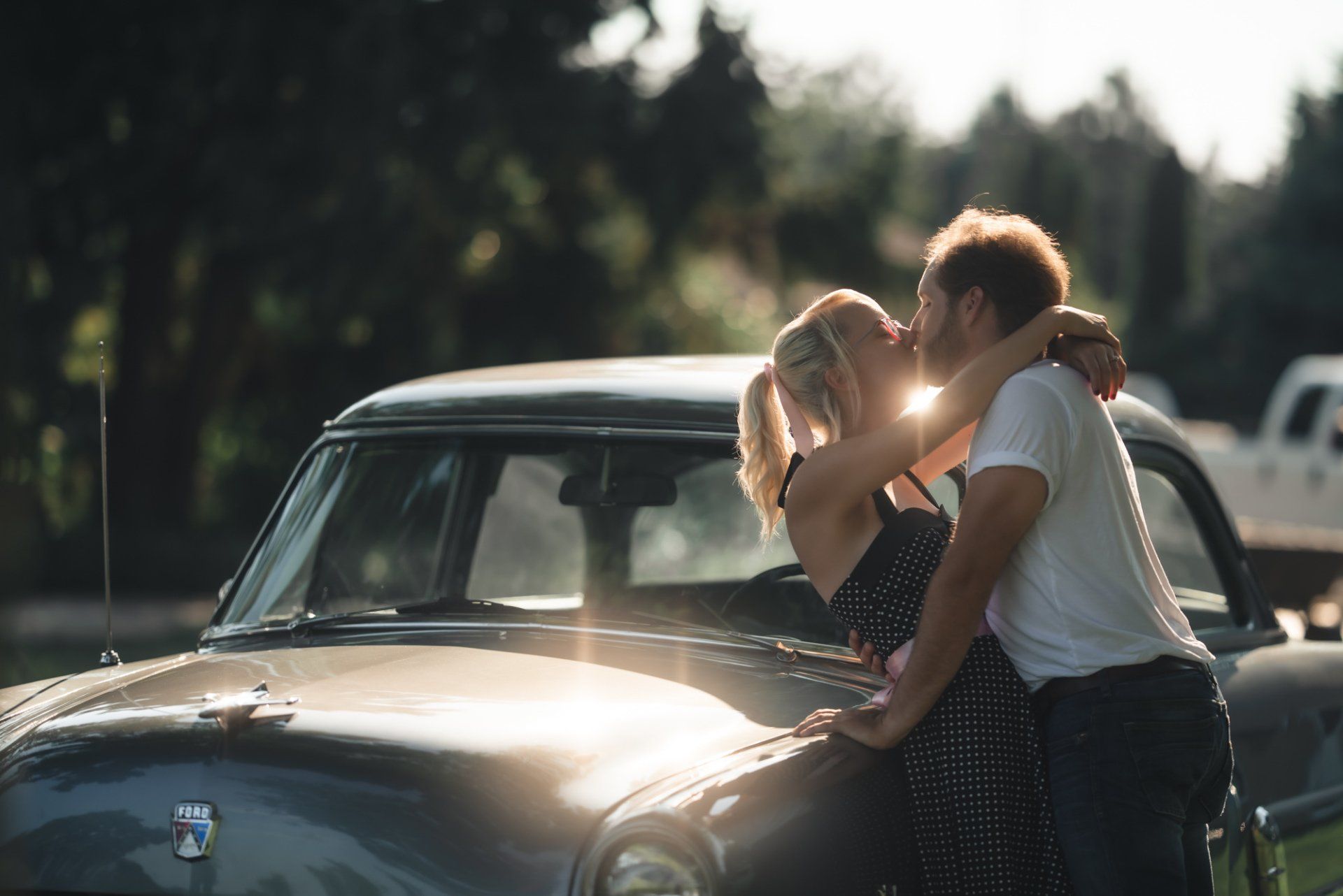A man and a woman are kissing in front of a car.