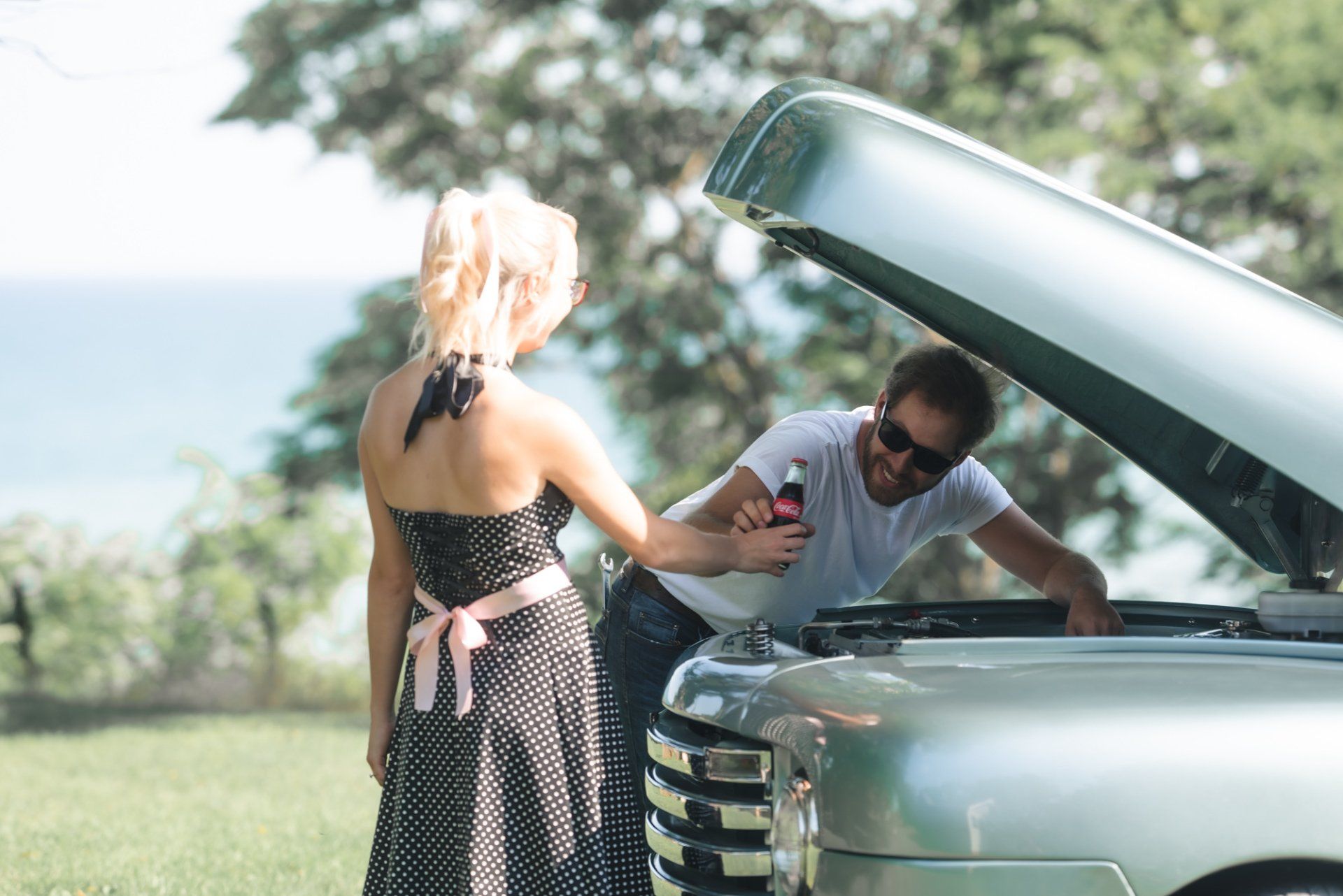 A man and a woman are looking under the hood of a car.