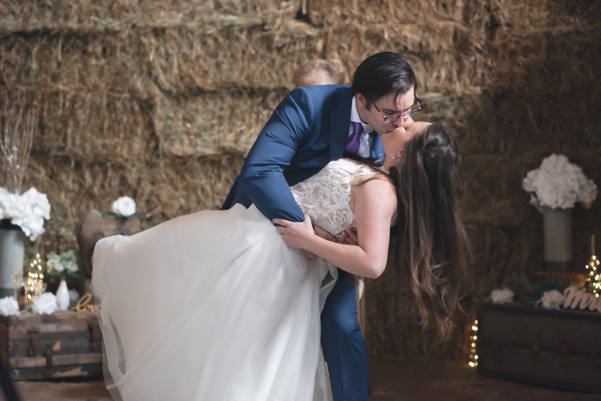 A bride and groom are kissing in front of a hay bale wall.