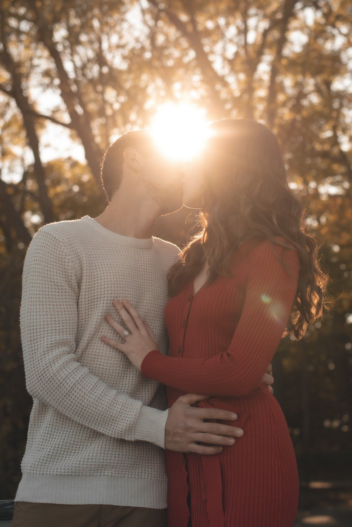 A man and a woman are kissing in front of the sun.
