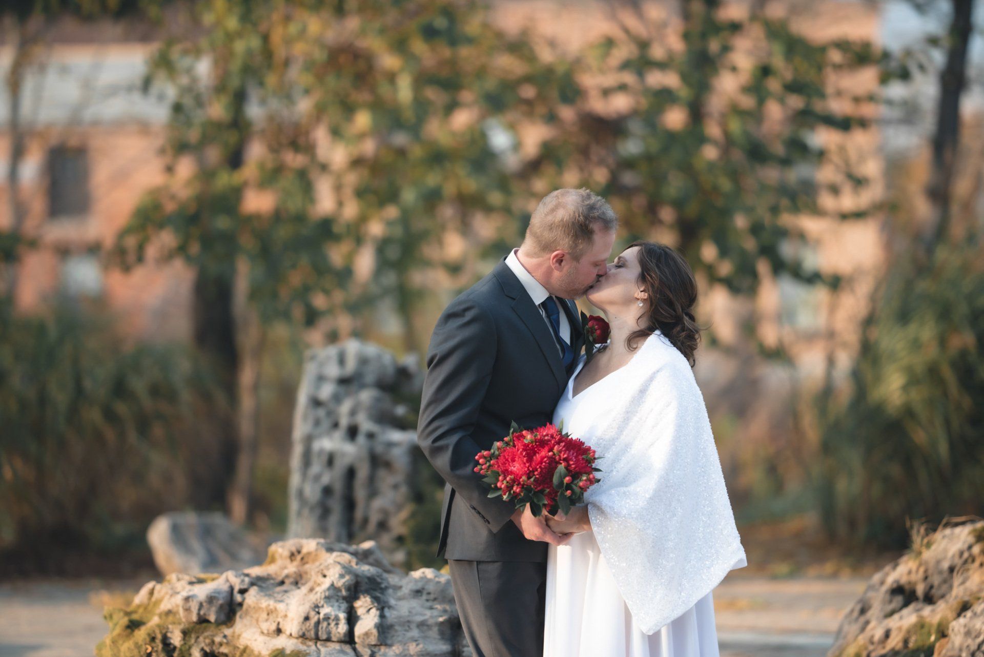 A bride and groom are kissing in front of a waterfall.