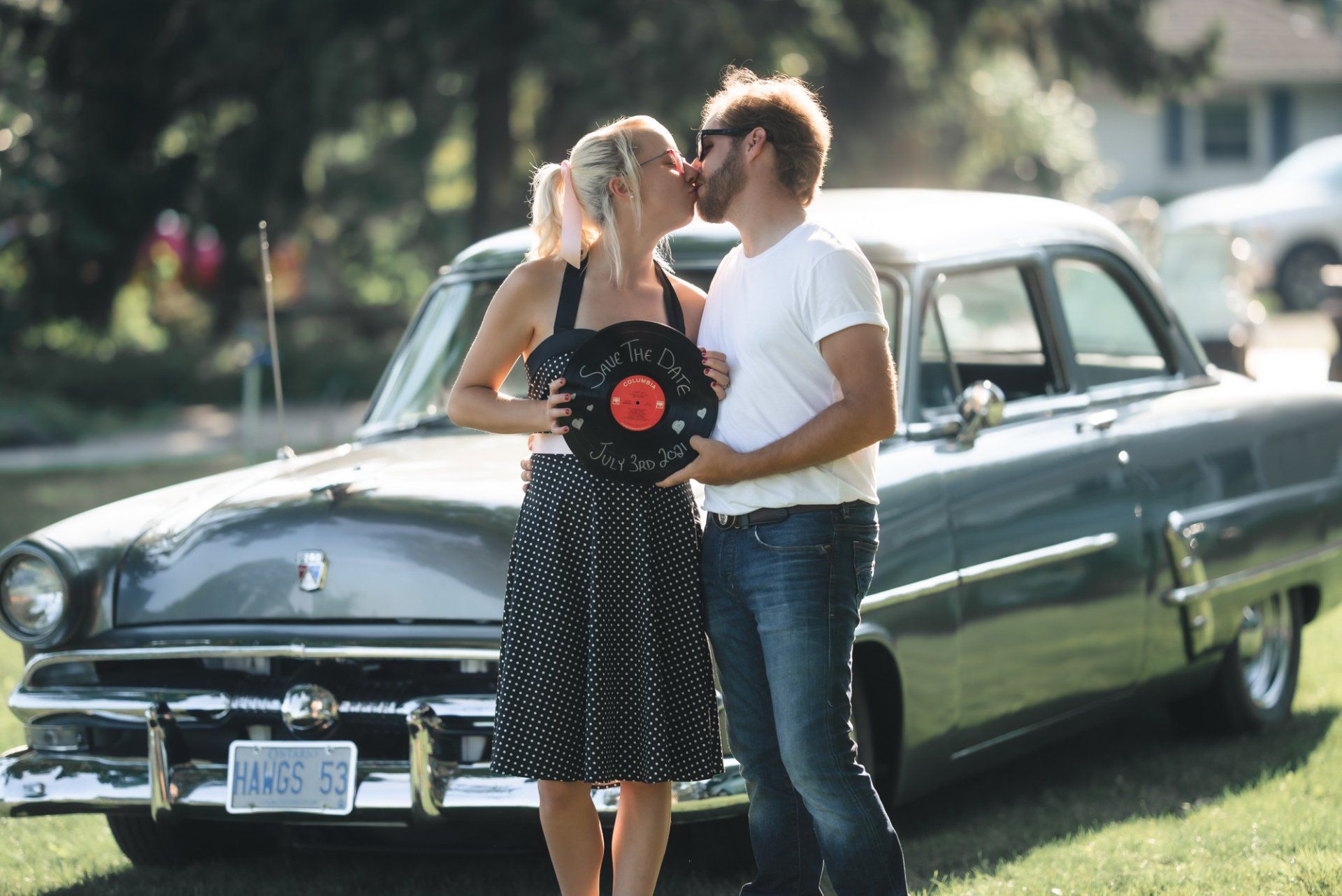A man and woman kissing in front of an old car