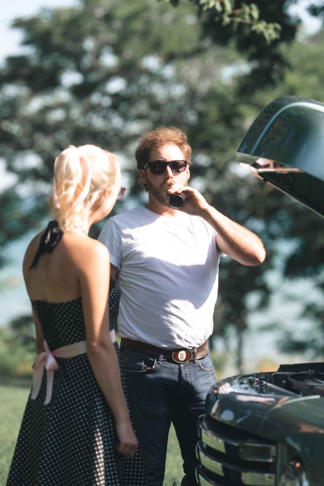 A man and a woman are standing next to a car with the hood open.