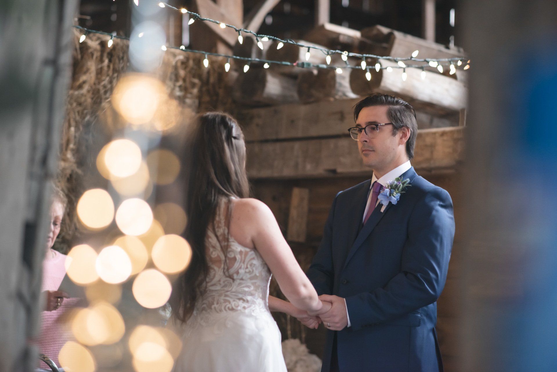 A bride and groom are holding hands during their wedding ceremony in a barn.