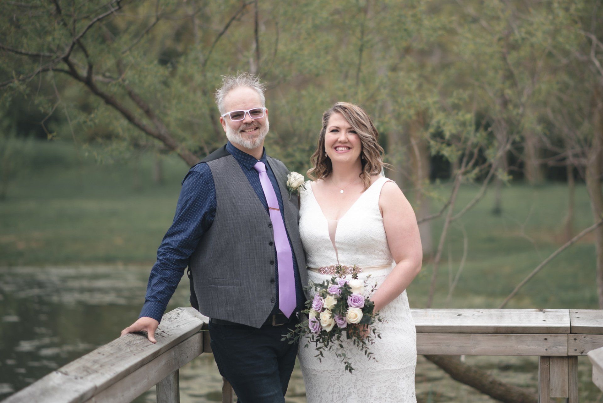 A bride and groom are posing for a picture on a wooden bridge.