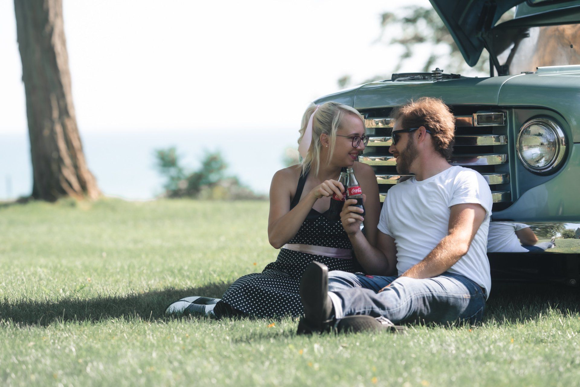 A man and a woman are sitting in the grass next to a car.