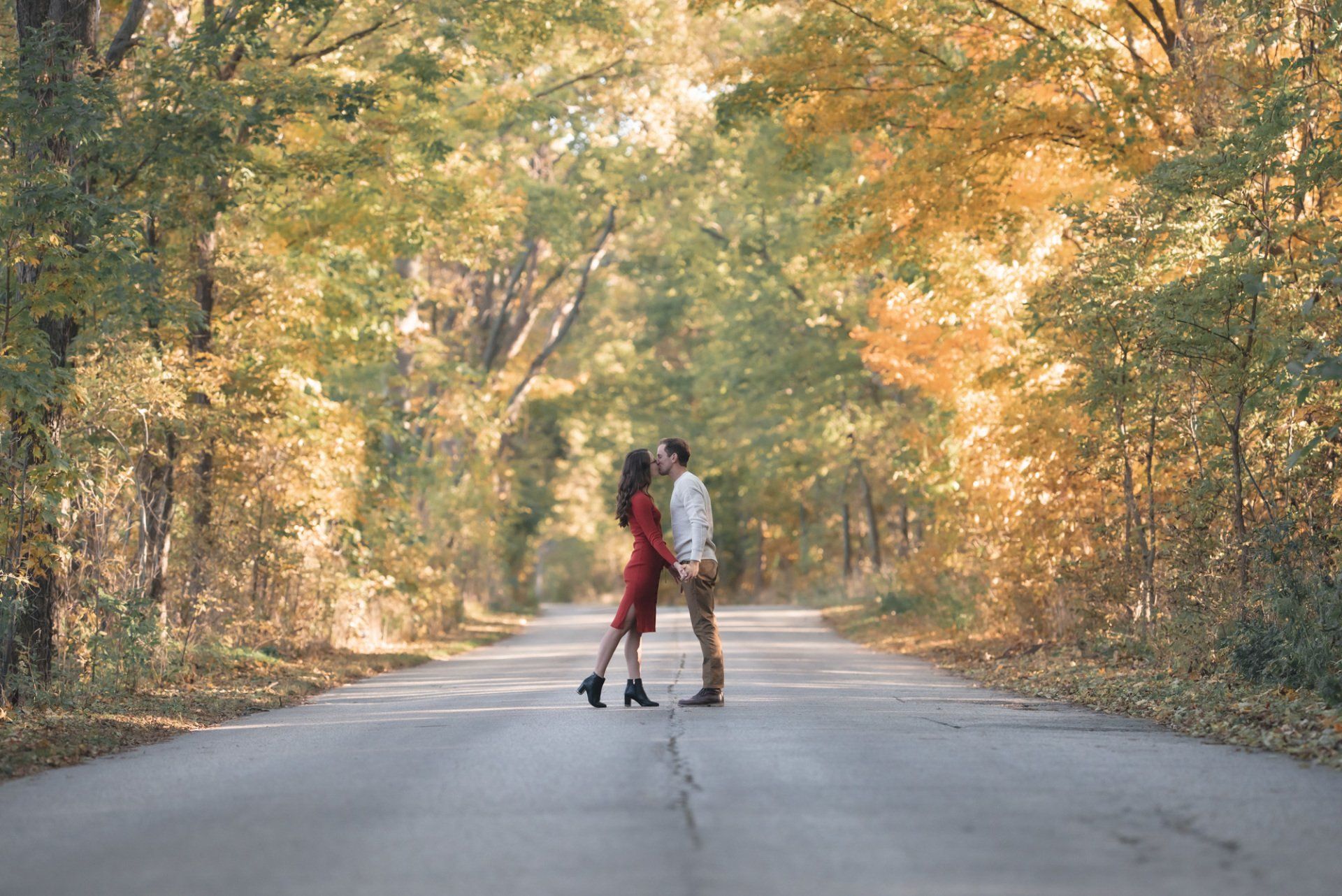 A man and a woman are kissing on the side of a road in the woods.
