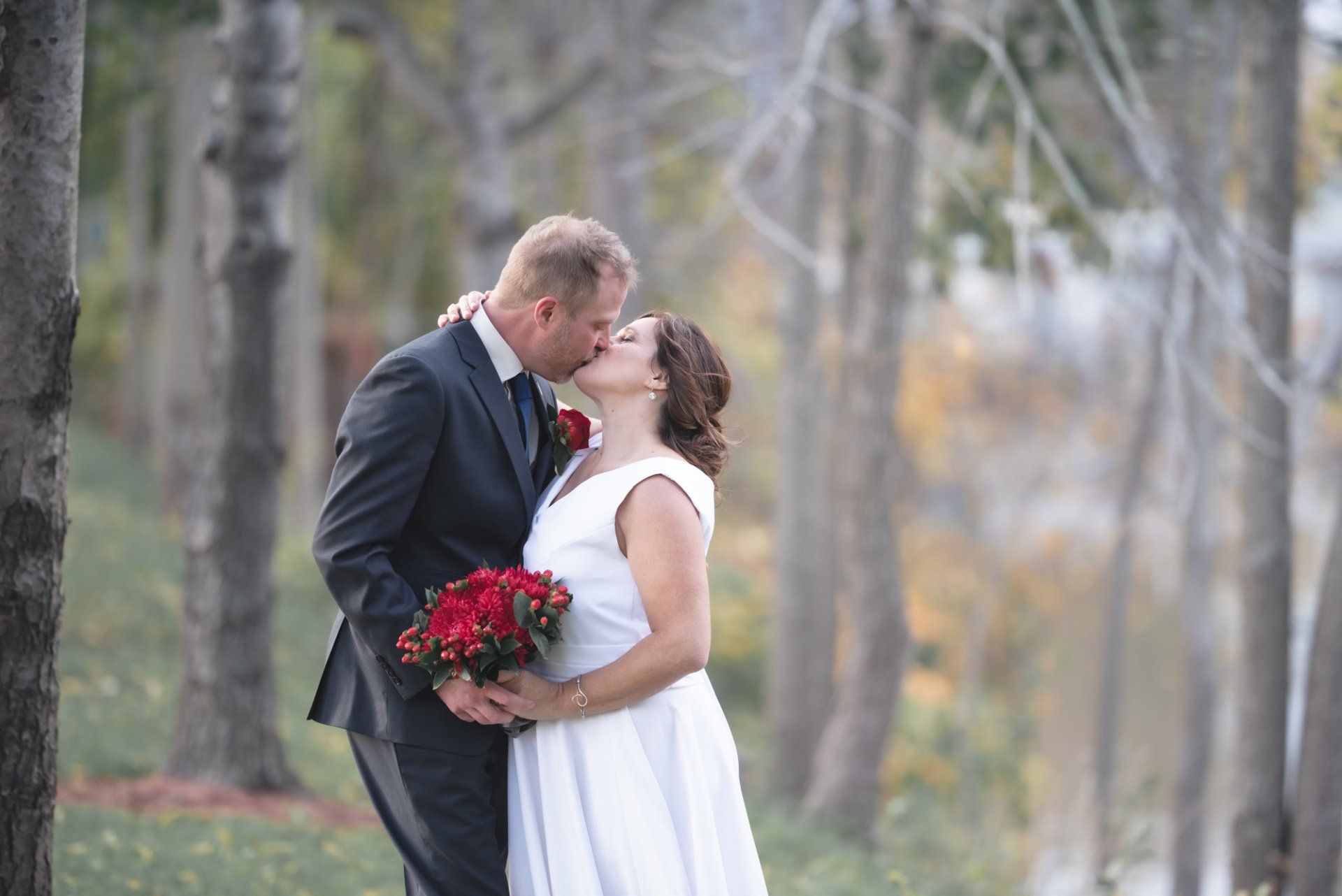 A bride and groom are kissing in the woods on their wedding day.