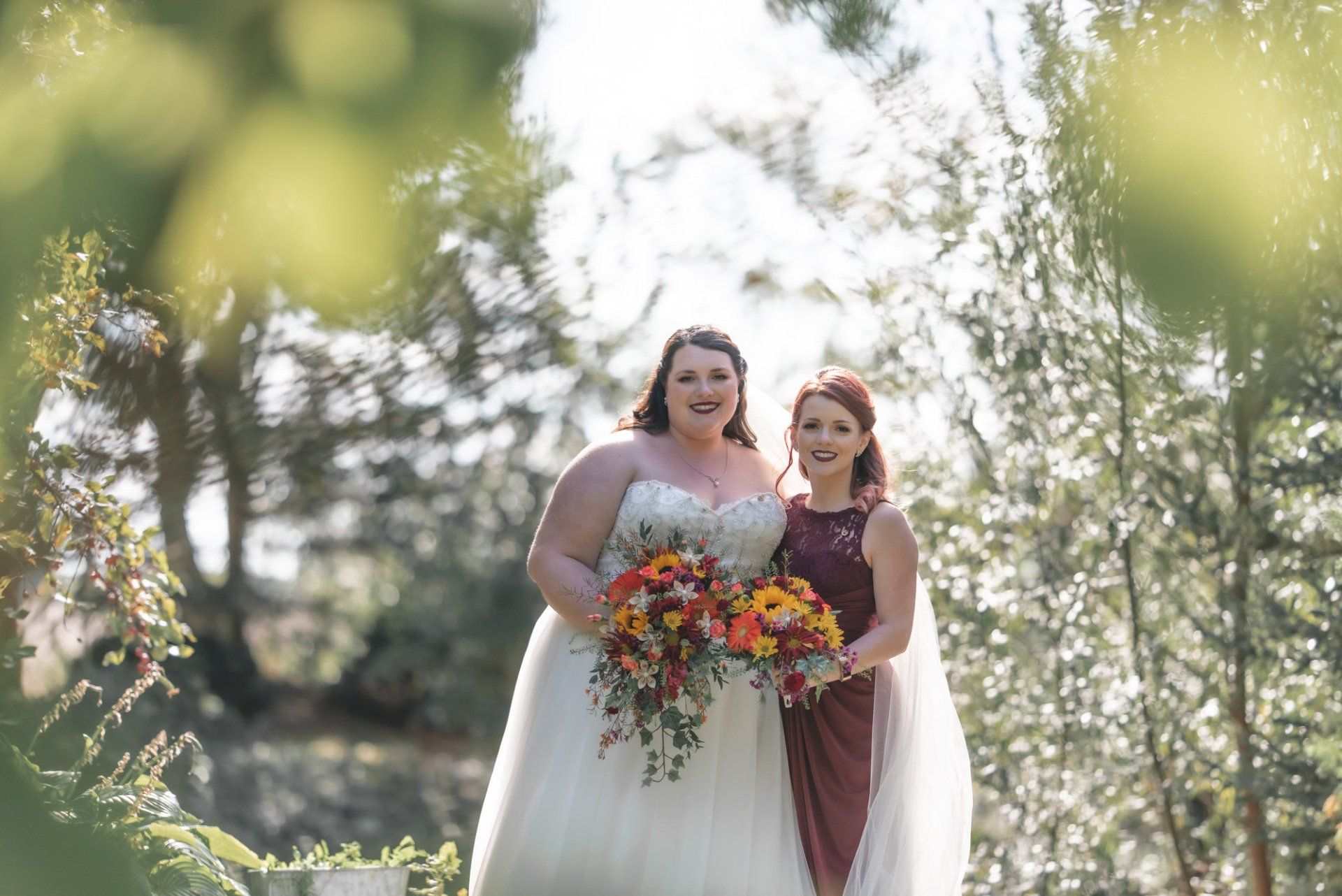 A bride and her bridesmaid are posing for a picture in the woods.