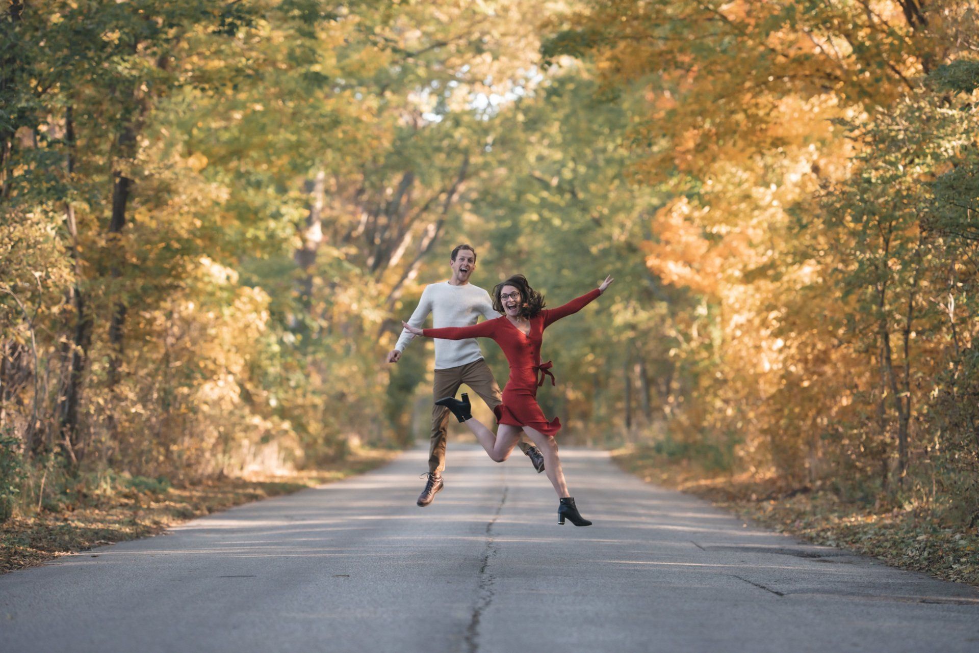 A man and a woman are jumping in the air on a road.