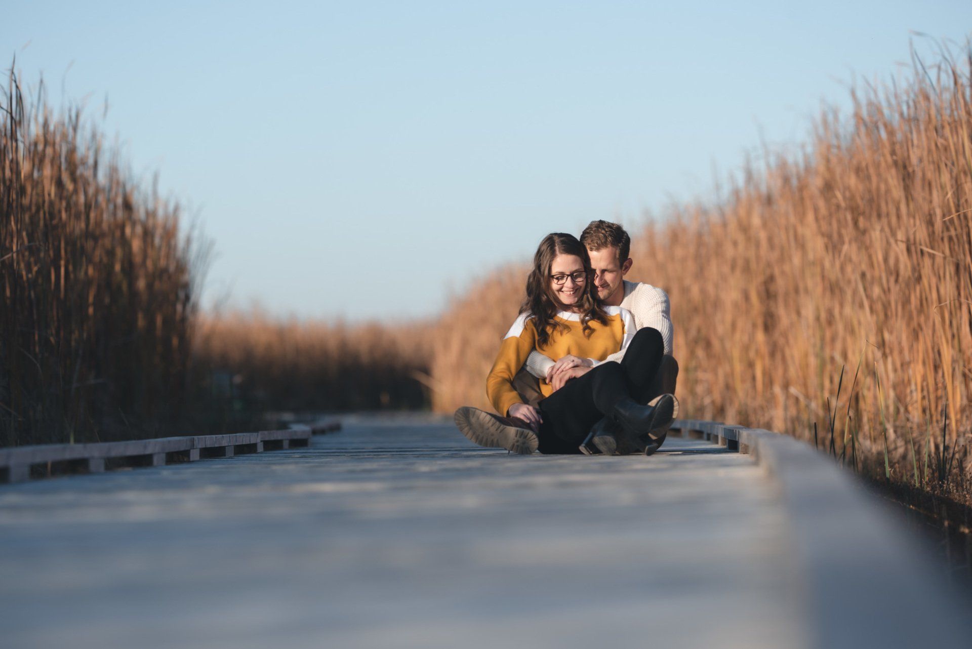 A man and a woman are sitting on a wooden boardwalk.