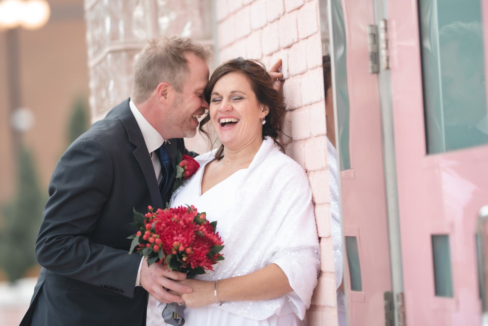 A bride and groom are posing for a picture in front of a pink door.