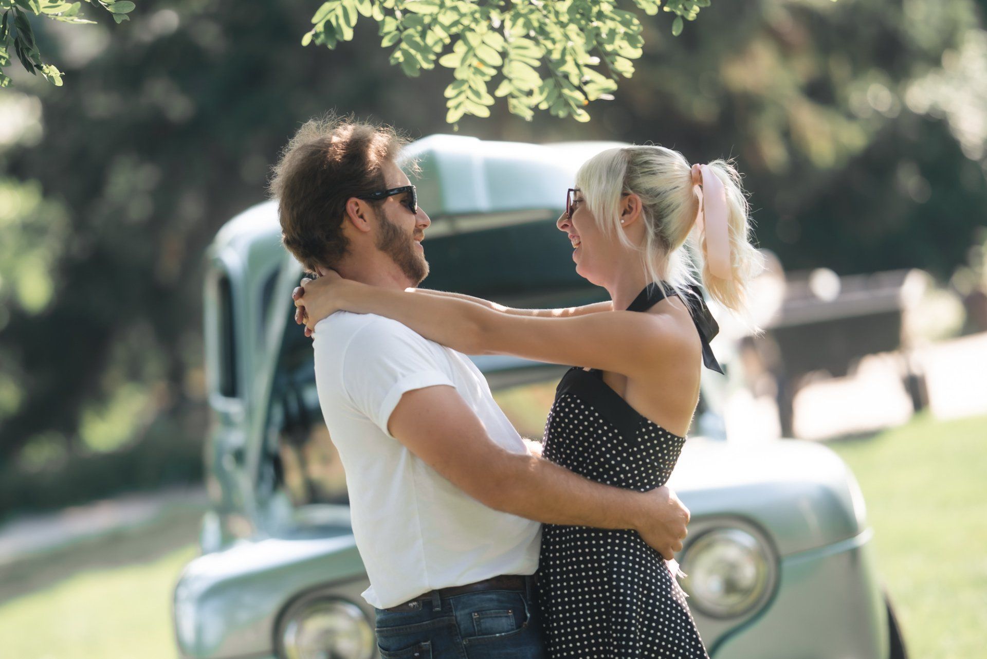 A man and a woman are hugging in front of a car.