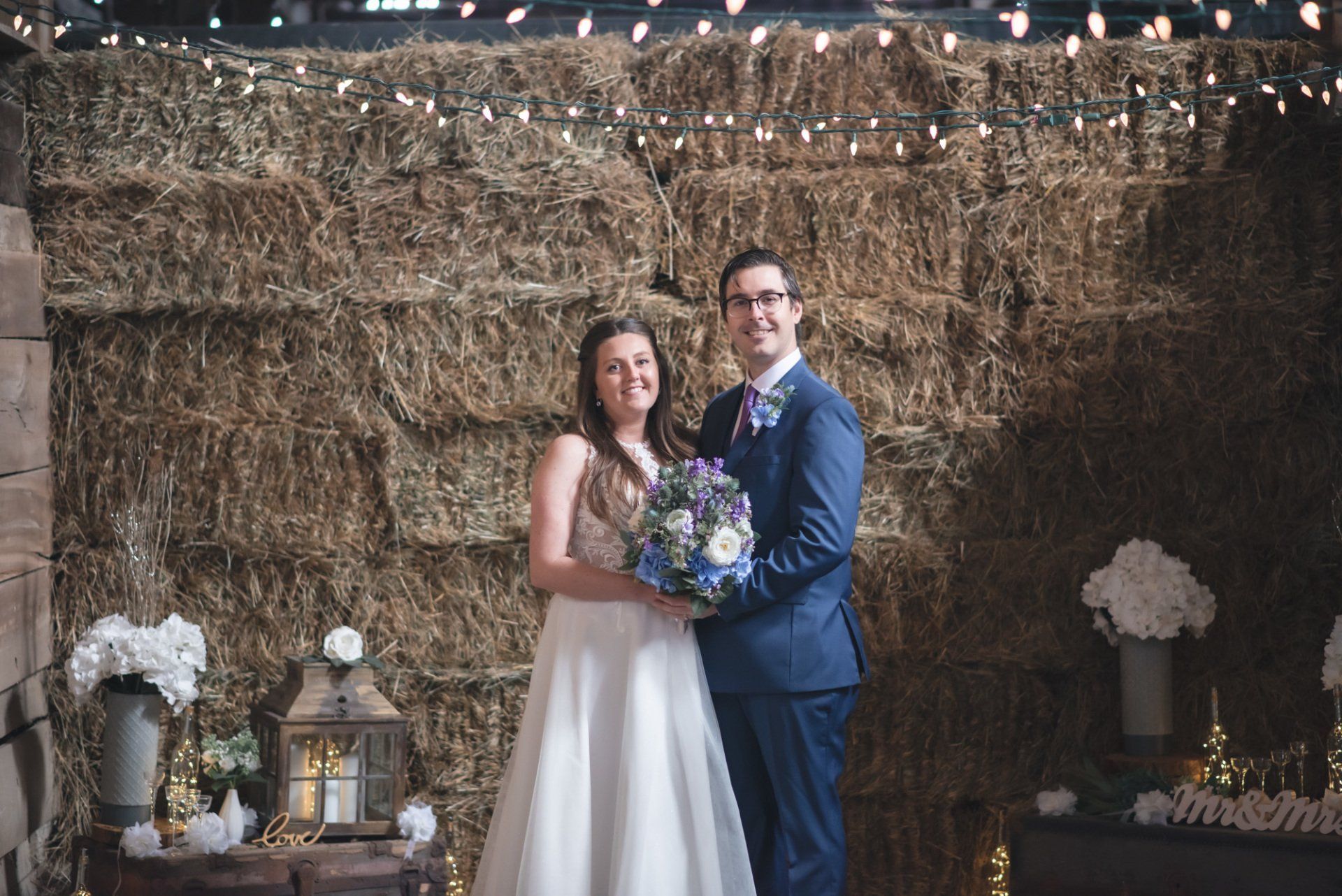 A bride and groom are posing for a picture in front of a hay bale wall.