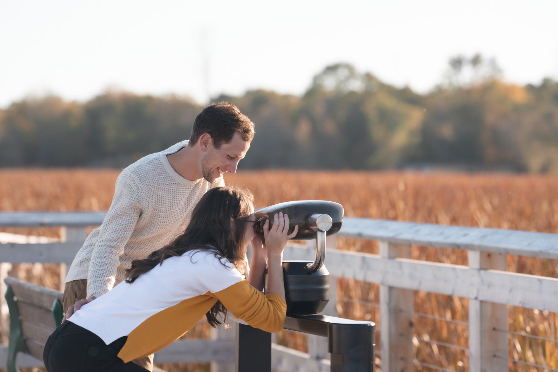 A man and a woman are looking through binoculars in a field.