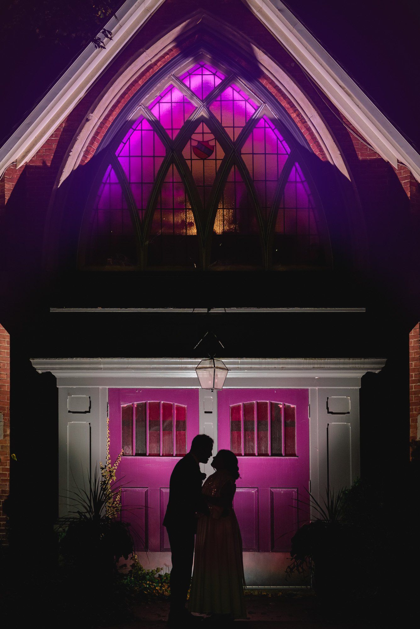A bride and groom are kissing in front of a church at night.