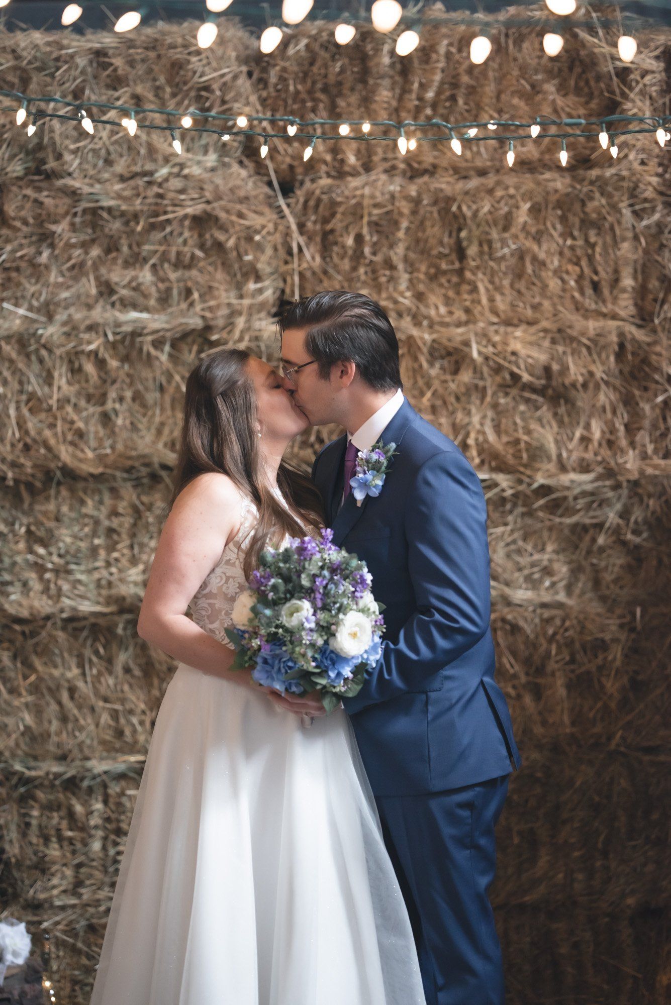 A bride and groom are kissing in front of hay bales.