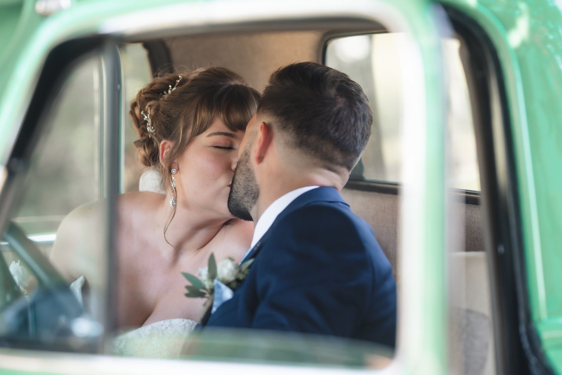 A bride and groom are kissing in the back of a green truck.