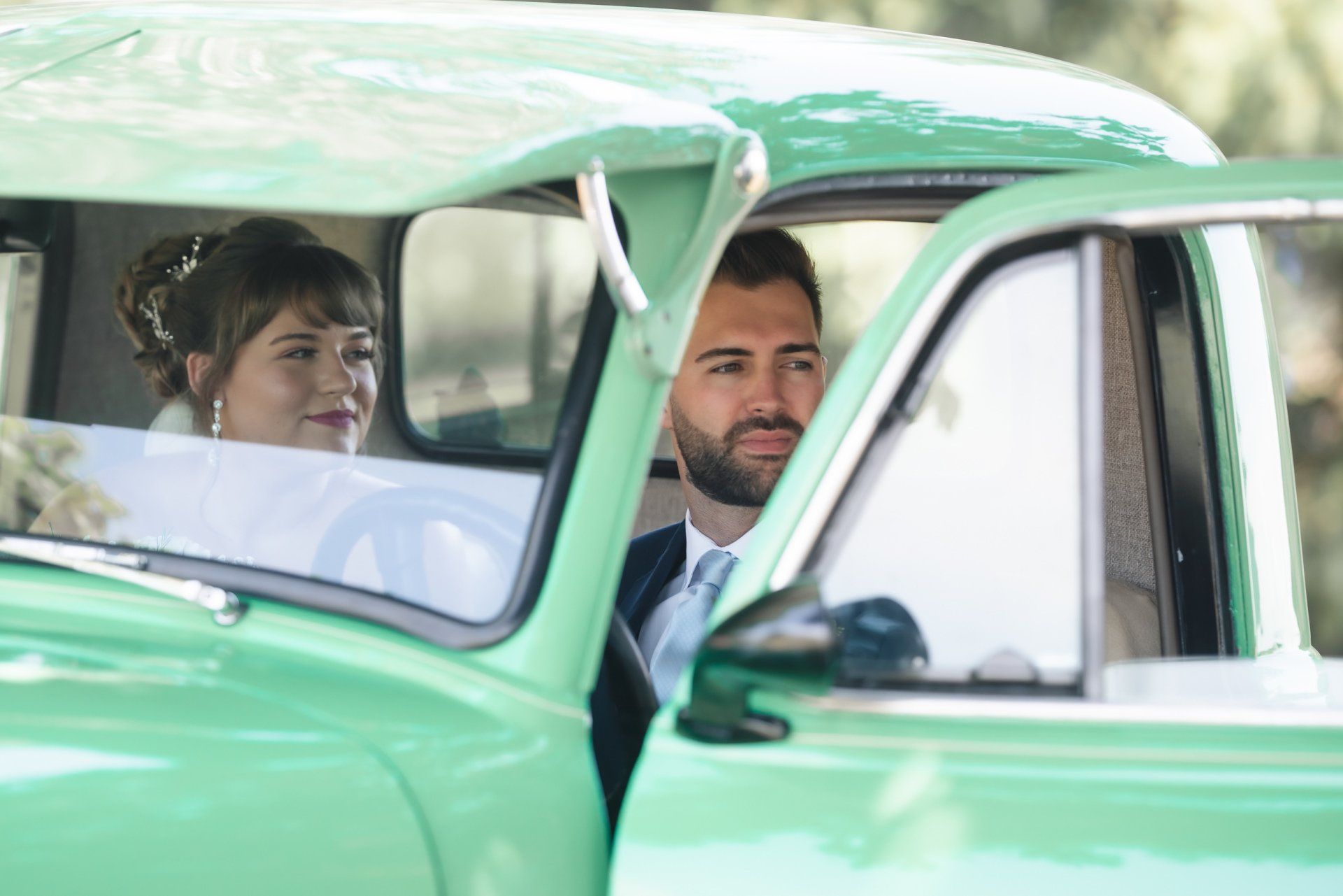 A bride and groom are sitting in a green car.