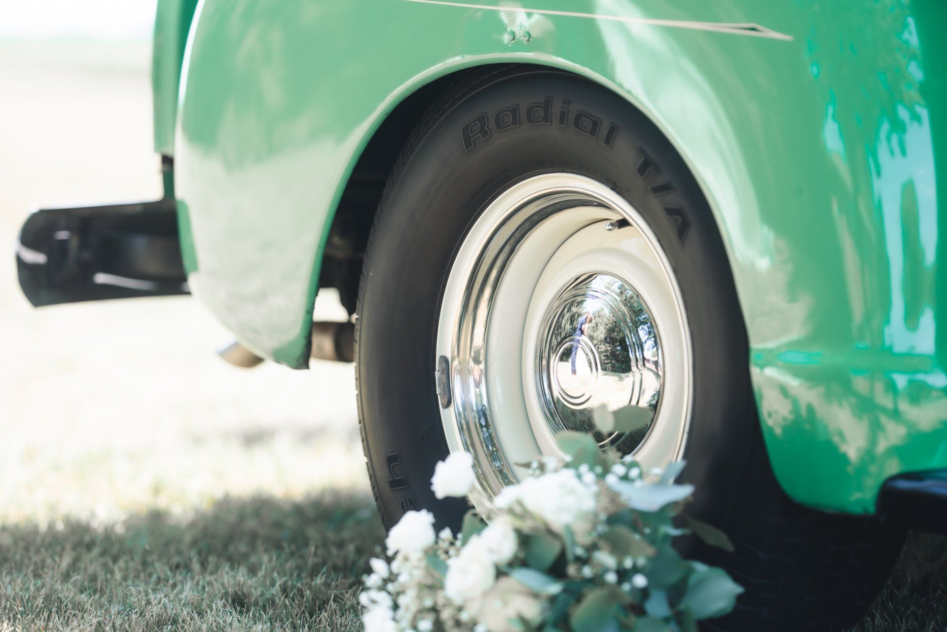 A green car with a radial tire is parked in the grass.