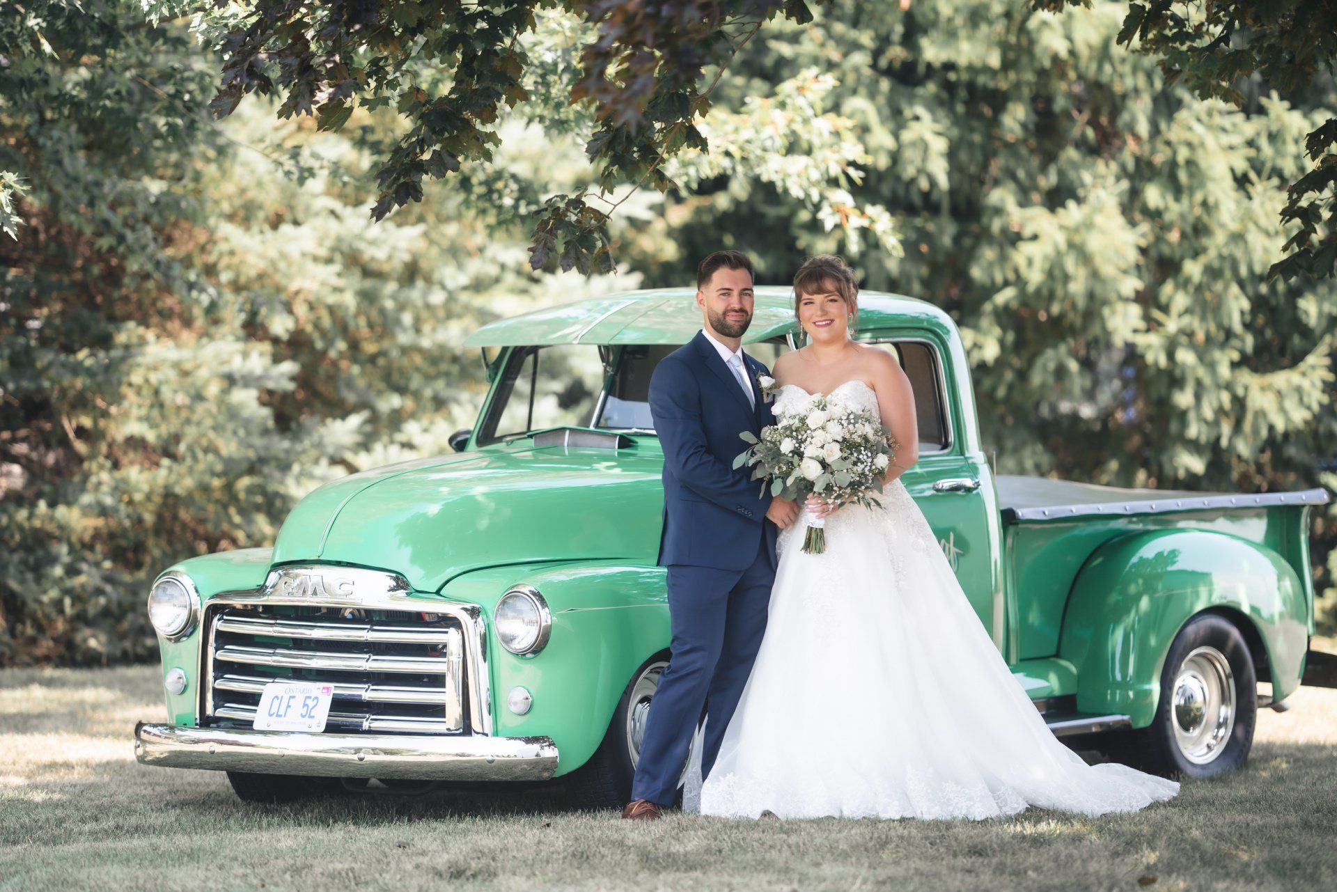 A bride and groom are posing for a picture in front of a green truck.