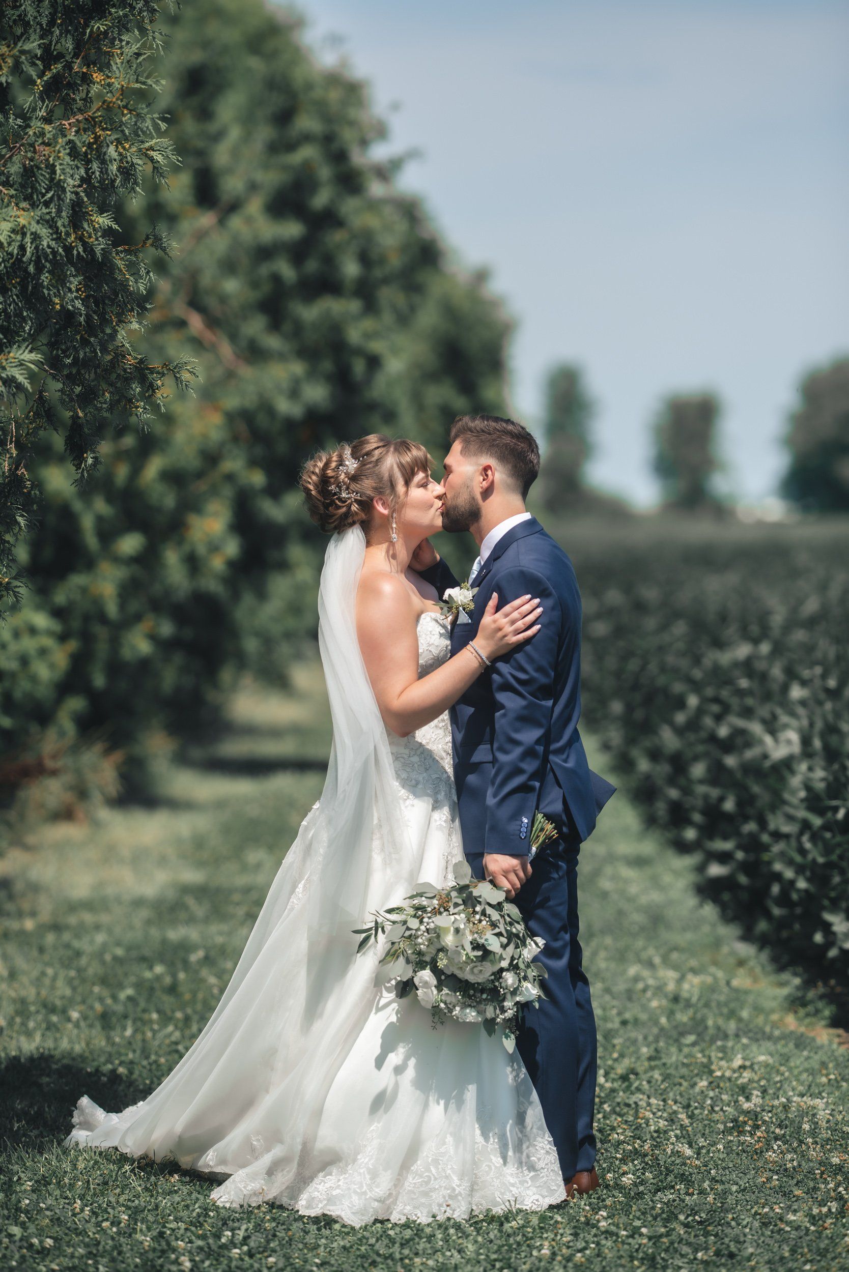 A bride and groom are kissing in a field of trees.