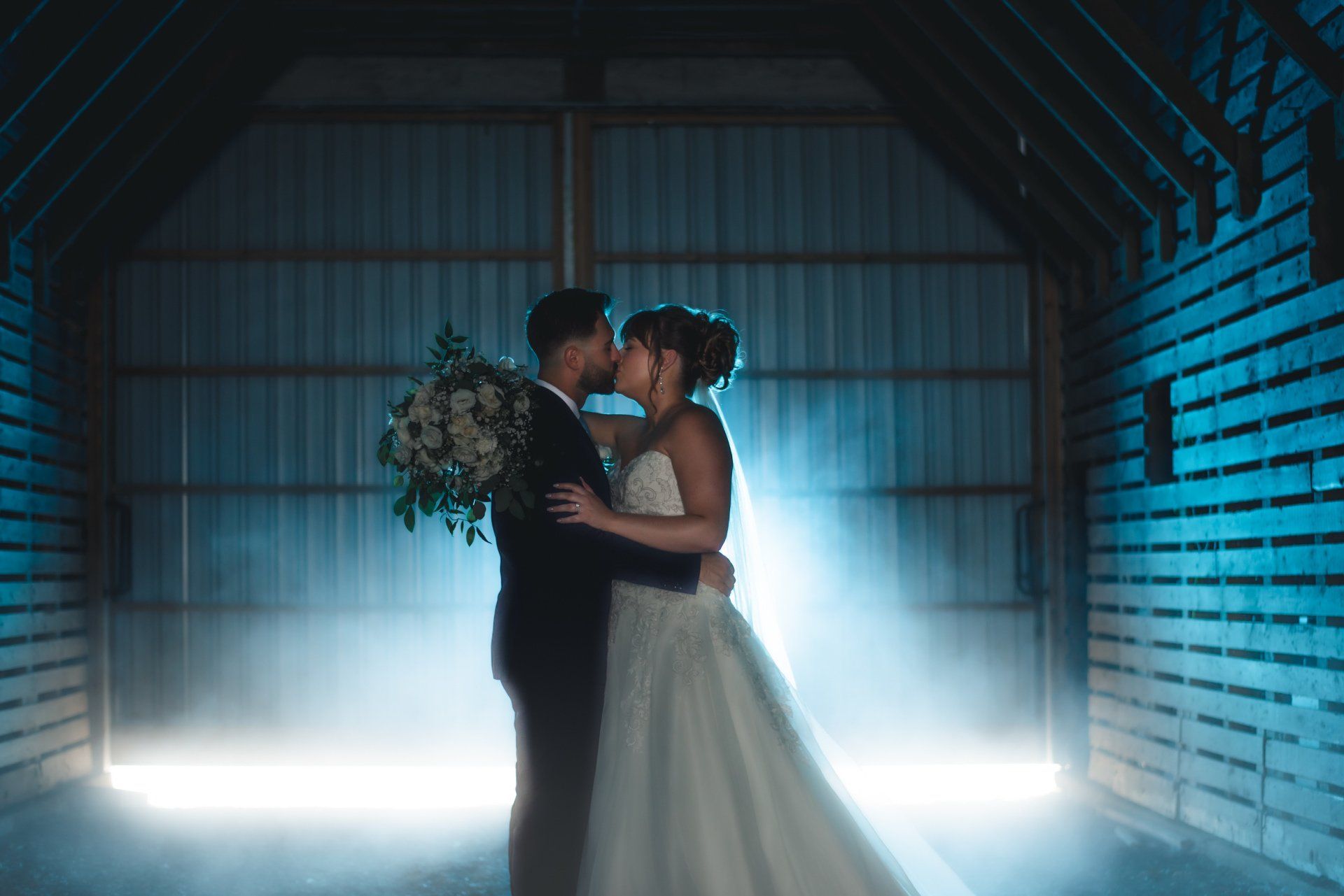 A bride and groom are kissing in a barn.