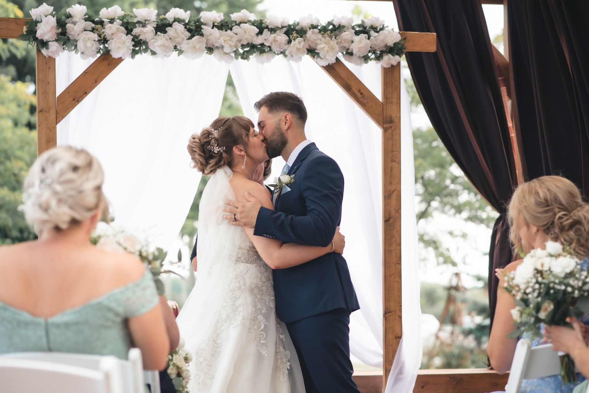 A bride and groom are kissing at their wedding ceremony.