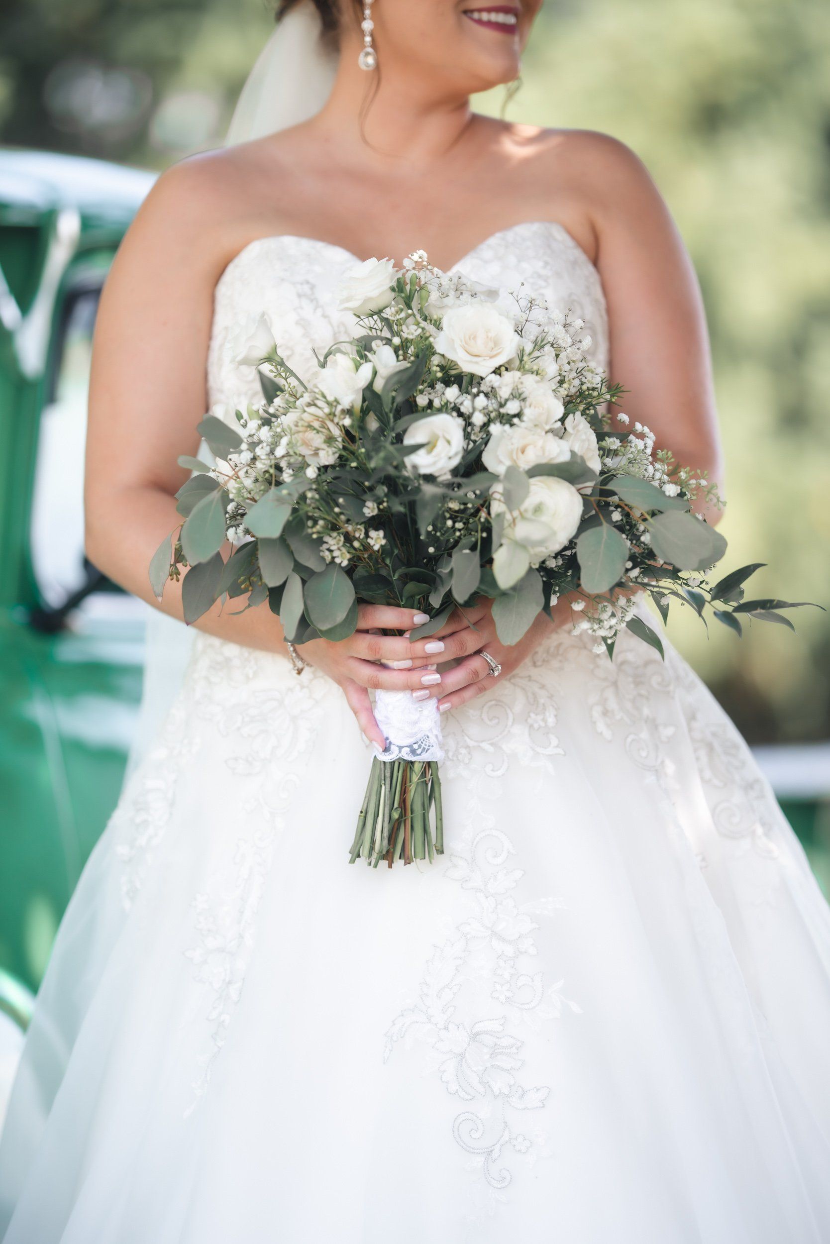A bride in a wedding dress is holding a bouquet of white flowers.