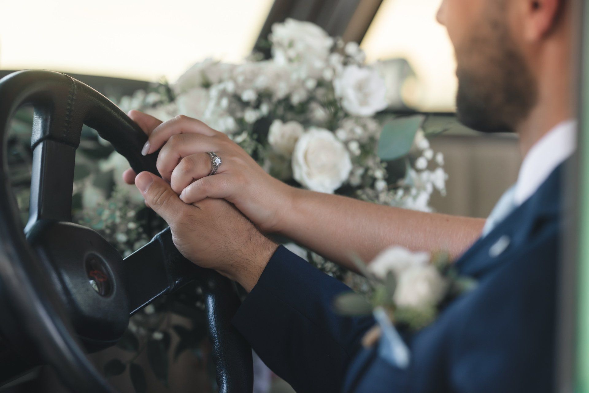 A bride and groom are holding hands while driving a car.