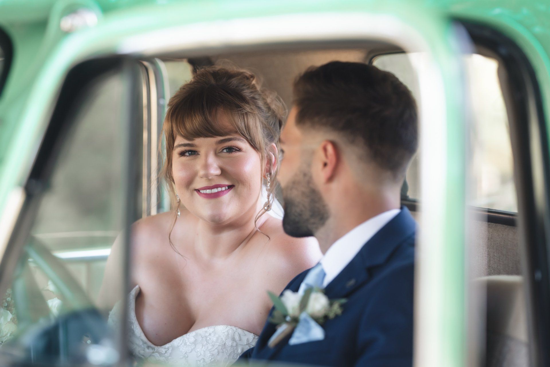 A bride and groom are sitting in the back seat of a green truck.