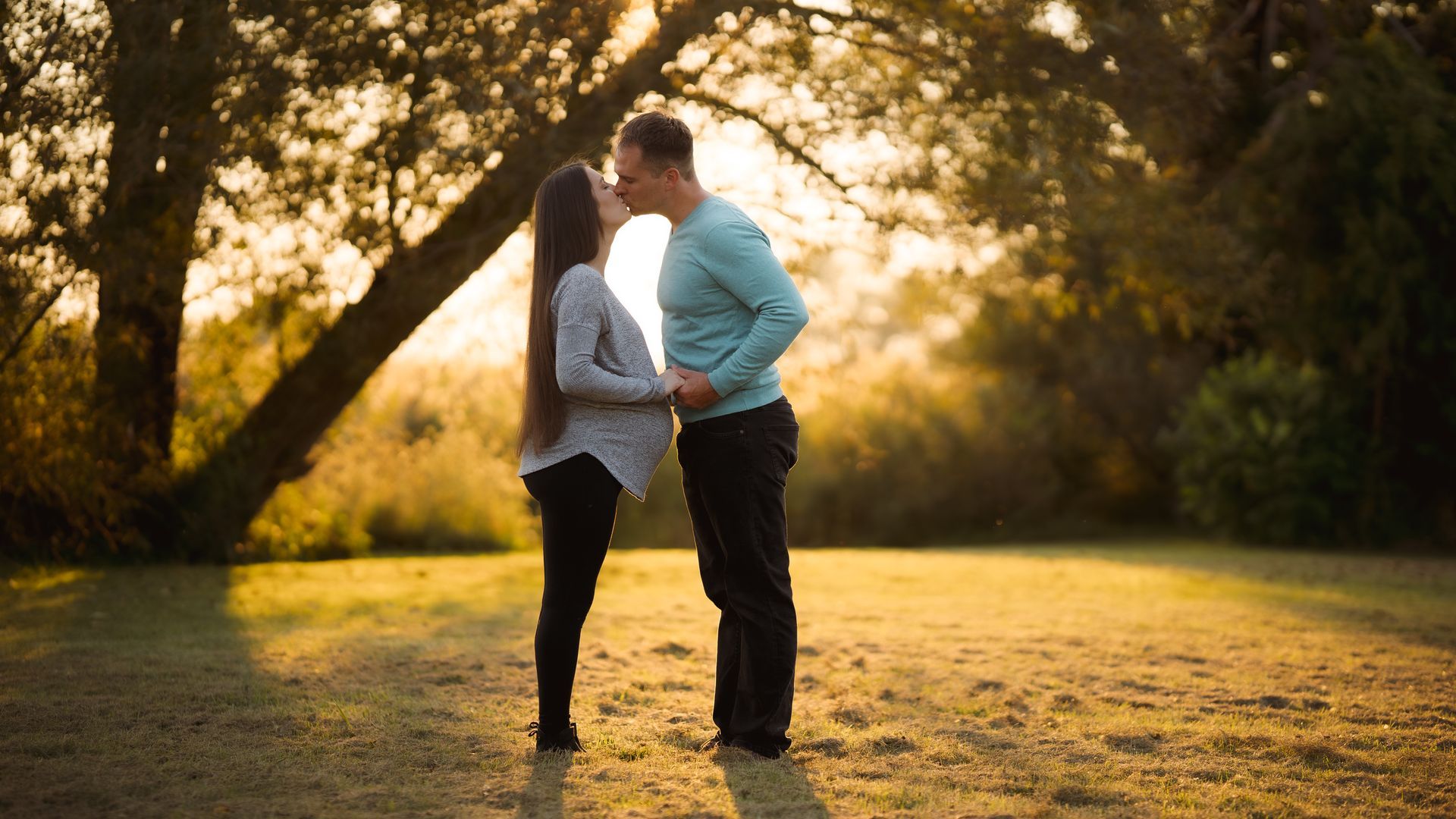 A man and a woman are kissing under a tree in a park.